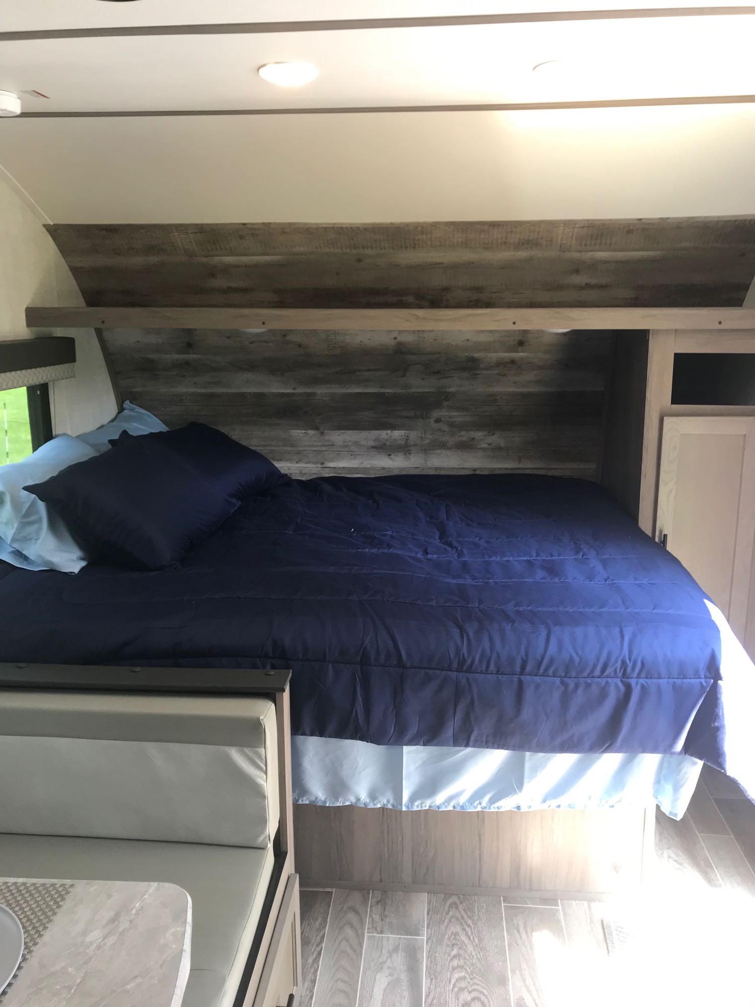 Inside a modern RV rental: A compact bedroom with a blue bed, rustic wood walls, and integrated storage. Dinette visible.. Gulf Stream Friendship 2022