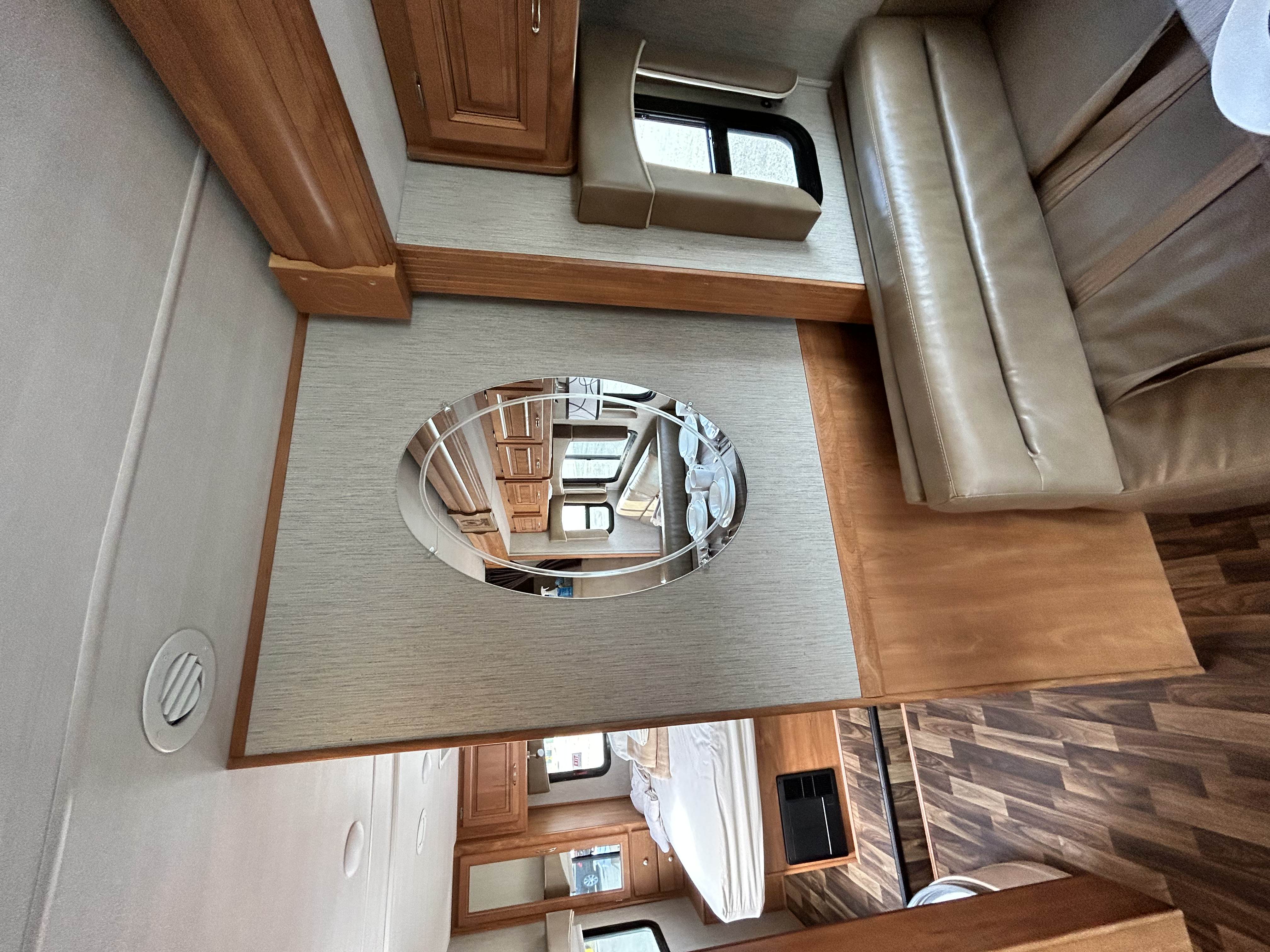 RV rental interior featuring a tan leather sofa, light walls with wood trim, and a mirror showing the bedroom area.. Nexus Phantom 2019