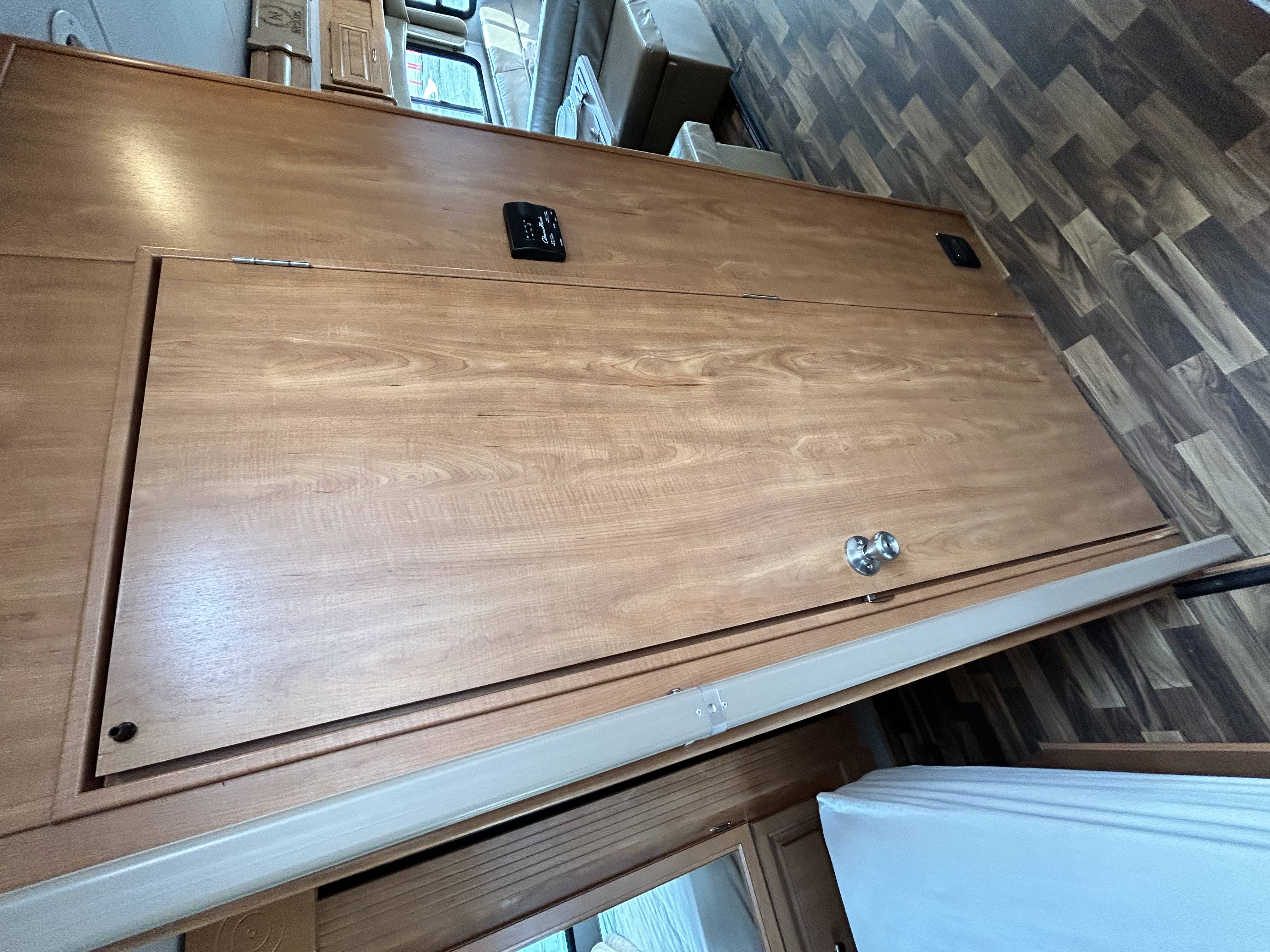 RV rental interior: a large wooden bed platform with a control panel, handle, and a mattress, next to wood-look flooring.. Nexus Phantom 2019