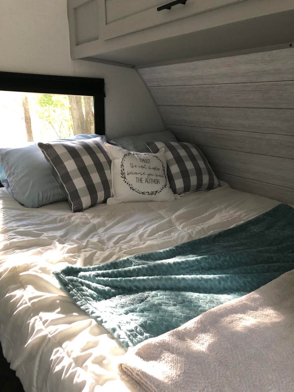 Relaxing RV rental bedroom: light-filled bed with checkered pillows, teal throw, and a window overlooking peaceful trees.. Forest River Wildwood FSX Platinum 2021