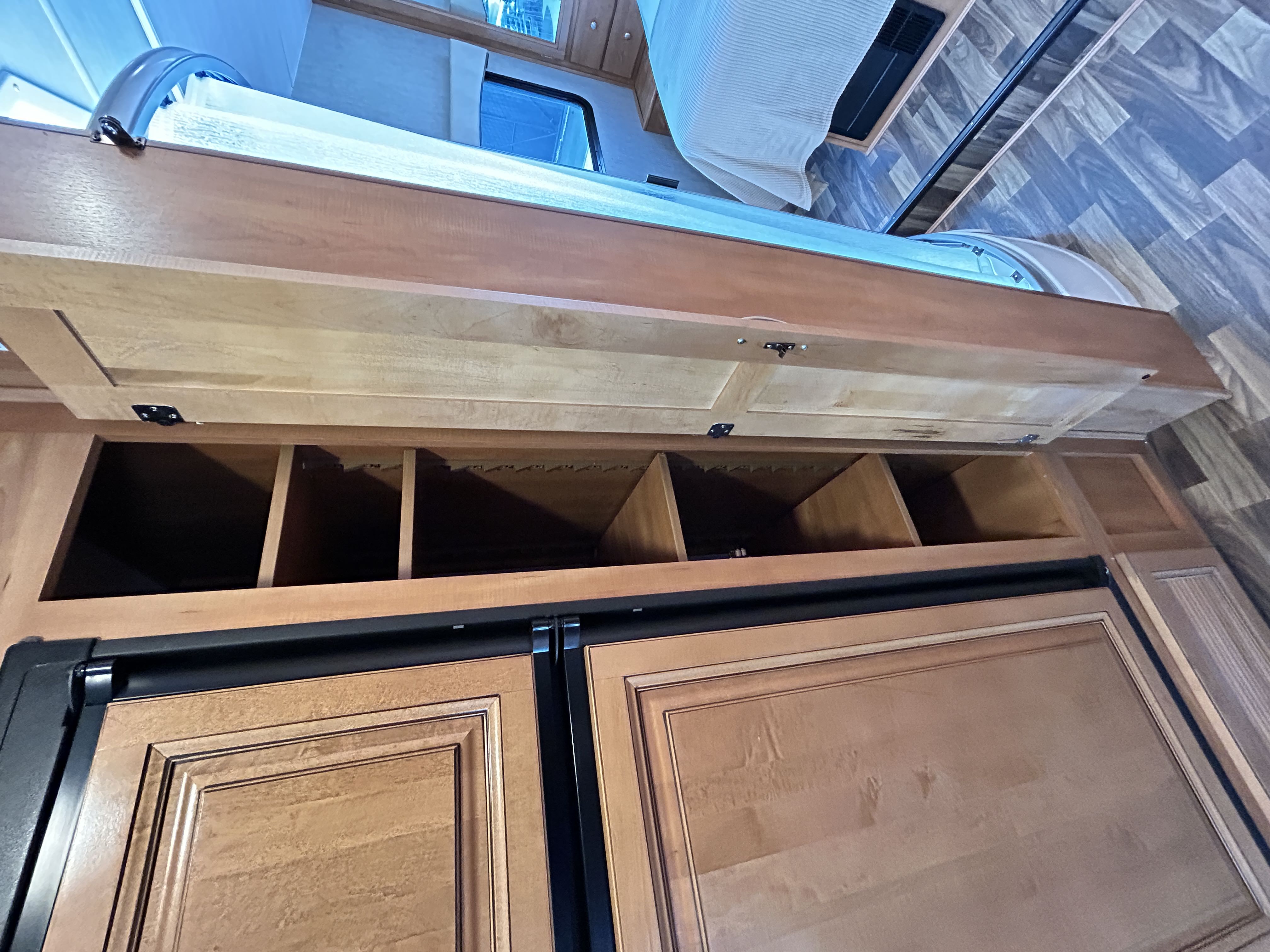RV rental interior: overhead bunk bed, open storage, and a large fridge with wood-look doors.. Nexus Phantom 2019