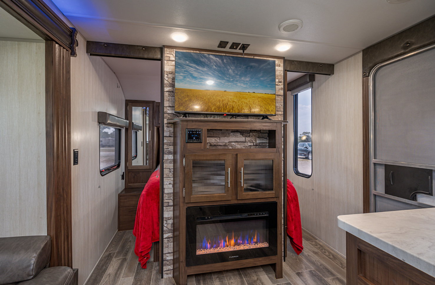 This RV rental offers a modern interior with a central entertainment unit, large TV, and electric fireplace, leading to the bedroom.. Forest River Cherokee Grey Wolf 2019