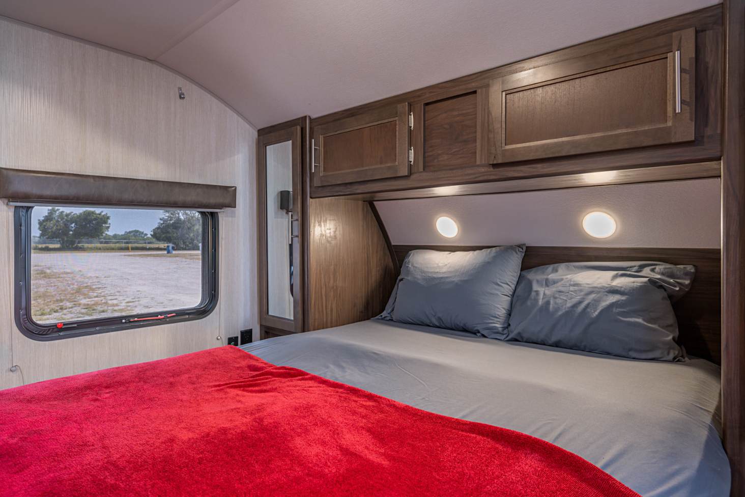 Cozy RV rental bedroom: bed with red blanket, grey sheets, overhead storage, and a scenic window view.. Forest River Cherokee Grey Wolf 2019