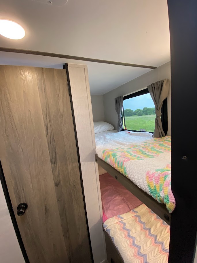 RV rental interior featuring cozy bunk beds with colorful blankets and a window view of a green field.. Gulf Stream Conquest Lite 2023