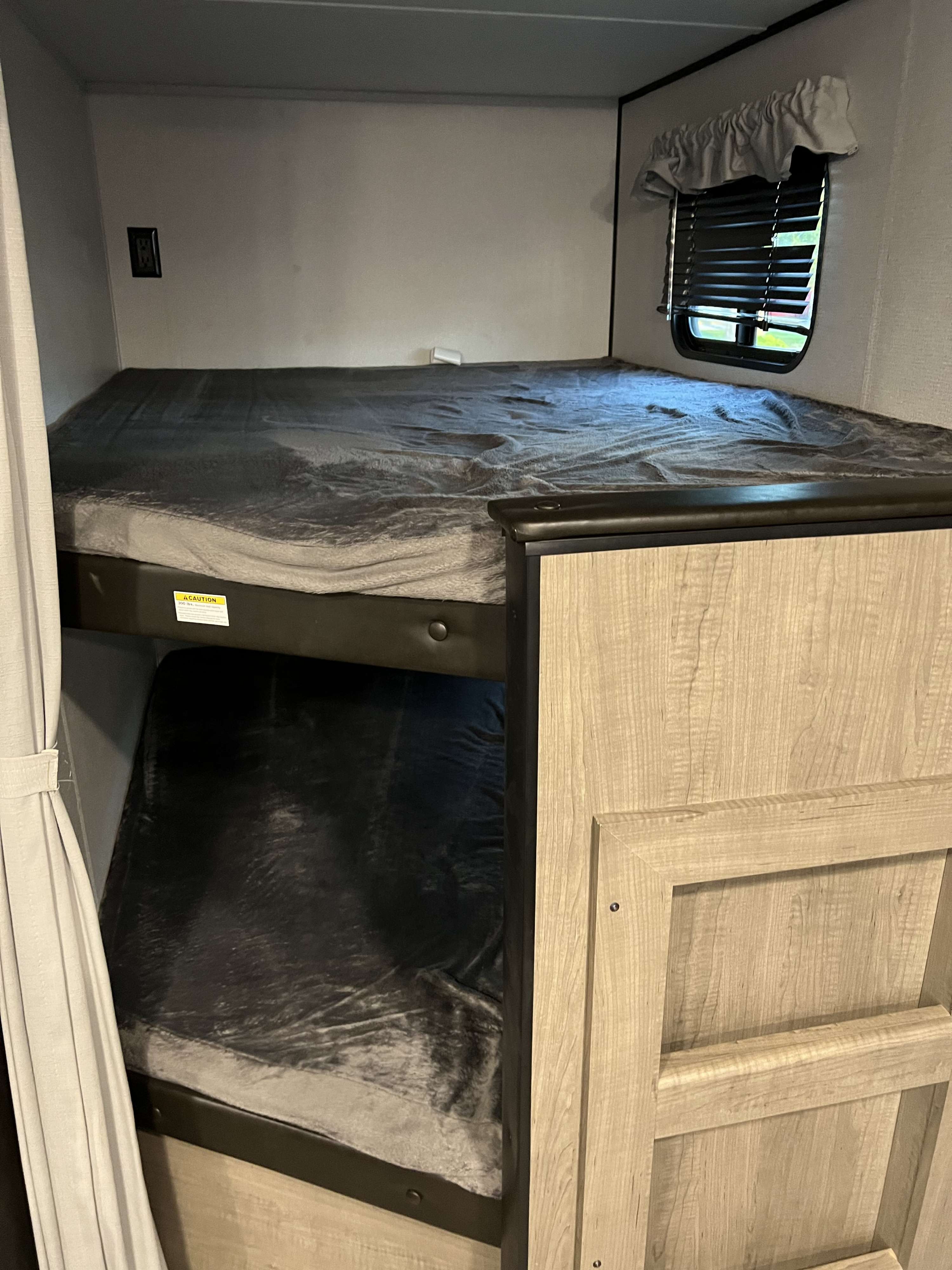 RV rental bunk beds: cozy interior sleeping area with upper/lower bunks, soft blankets, window, and outlets.. Keystone RV Other 2021