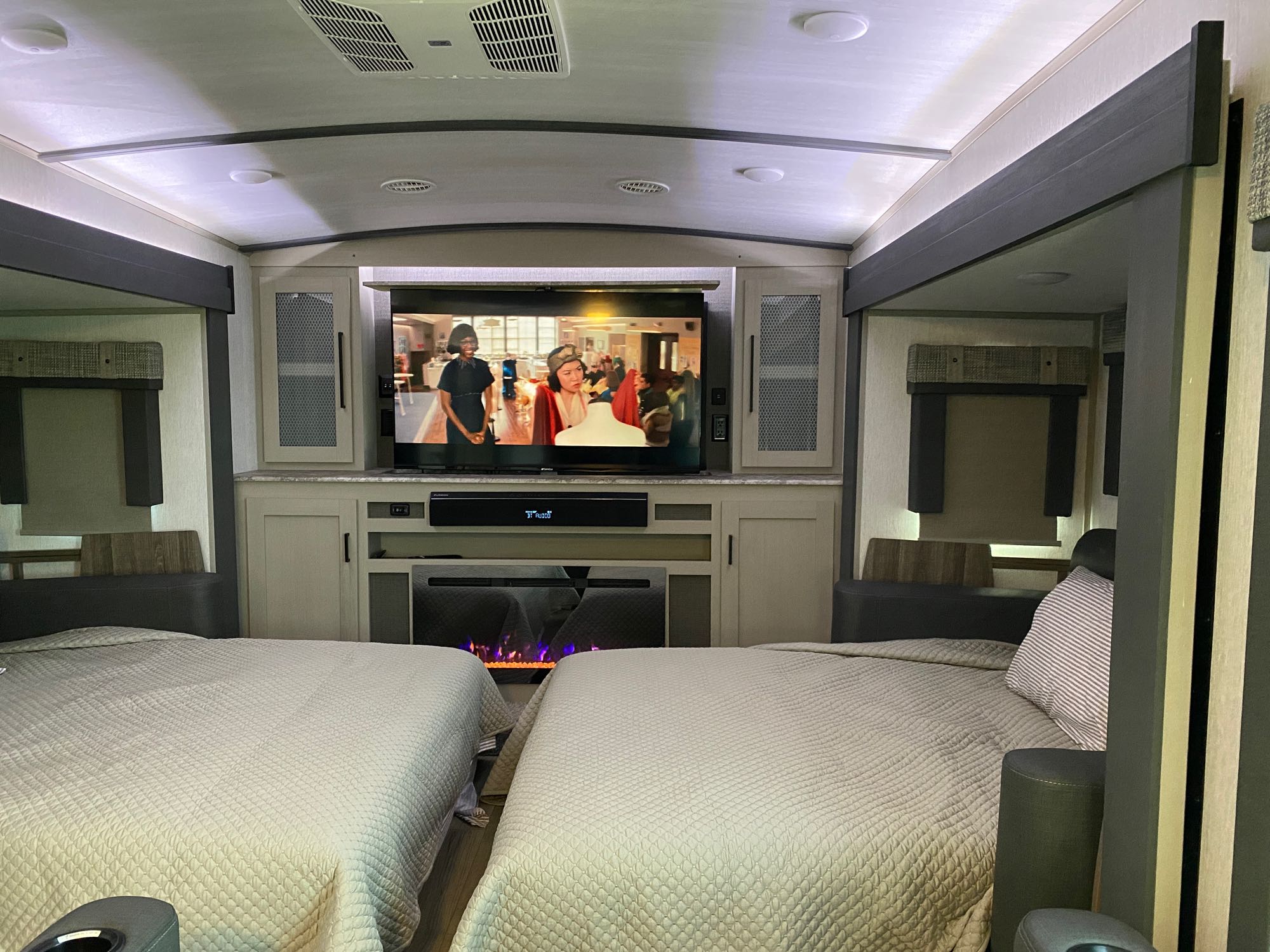 Cozy RV rental interior featuring two beds, a large TV, soundbar, and electric fireplace, ideal for family trips.. Forest River Heritage Glen Elite 2023
