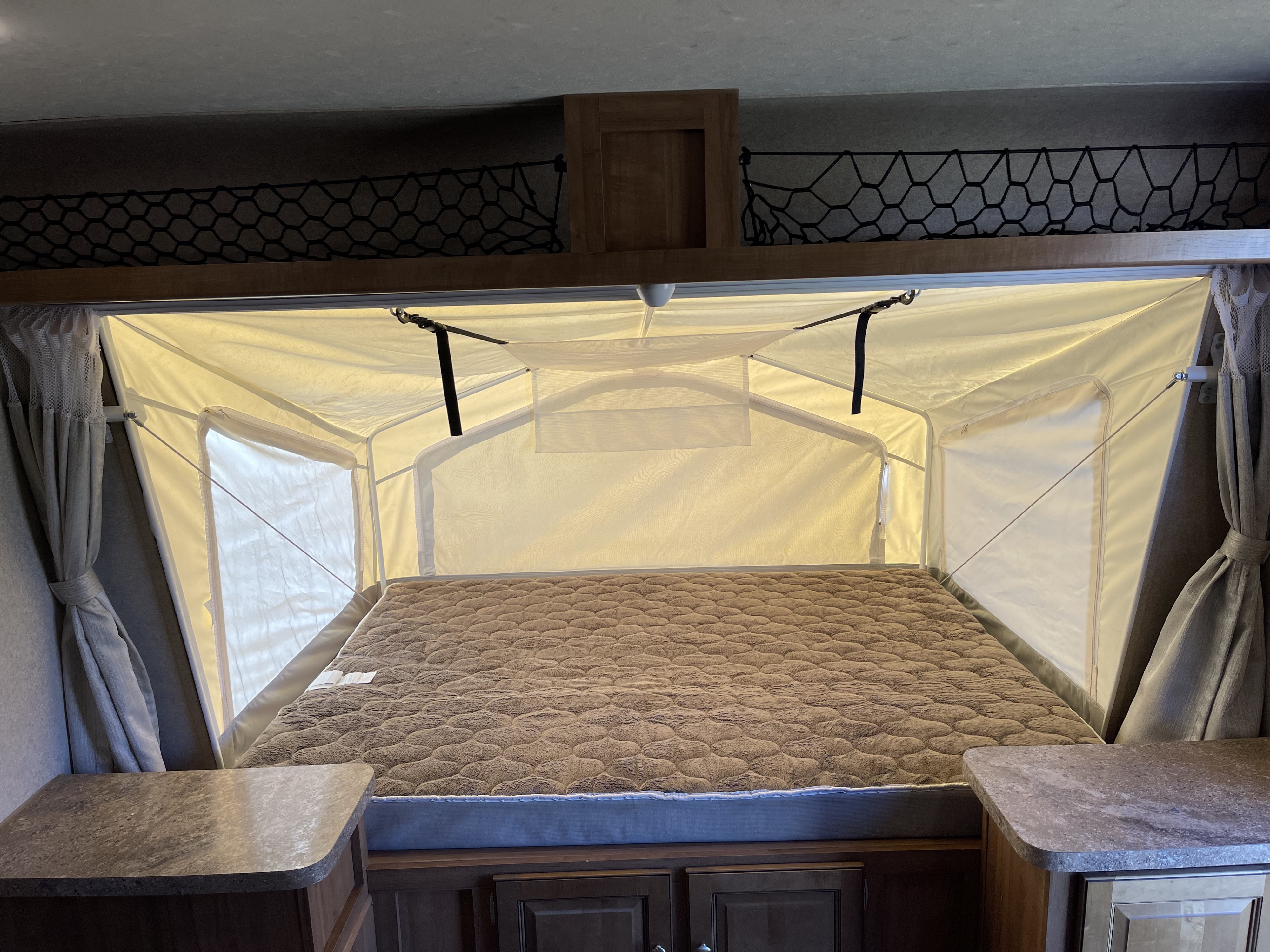 Interior of an RV rental showing a plush pop-out bed with fabric walls and nets for comfortable overnight stays.. Forest River Rockwood Roo 2019