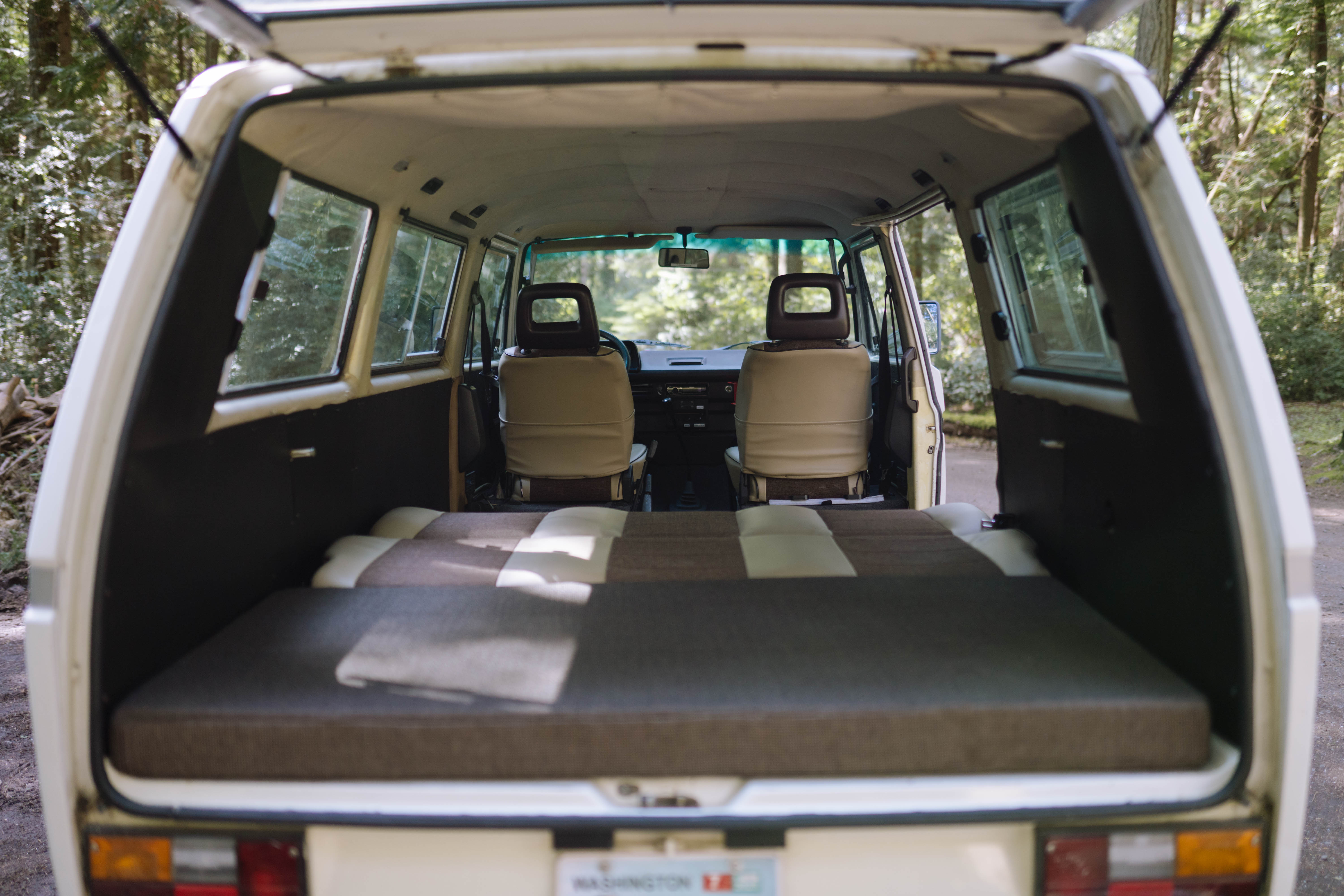Cozy camper van interior viewed from the rear, with a bed laid out and front seats visible. Ideal for an RV rental adventure.. Volkswagen Syncro 1987