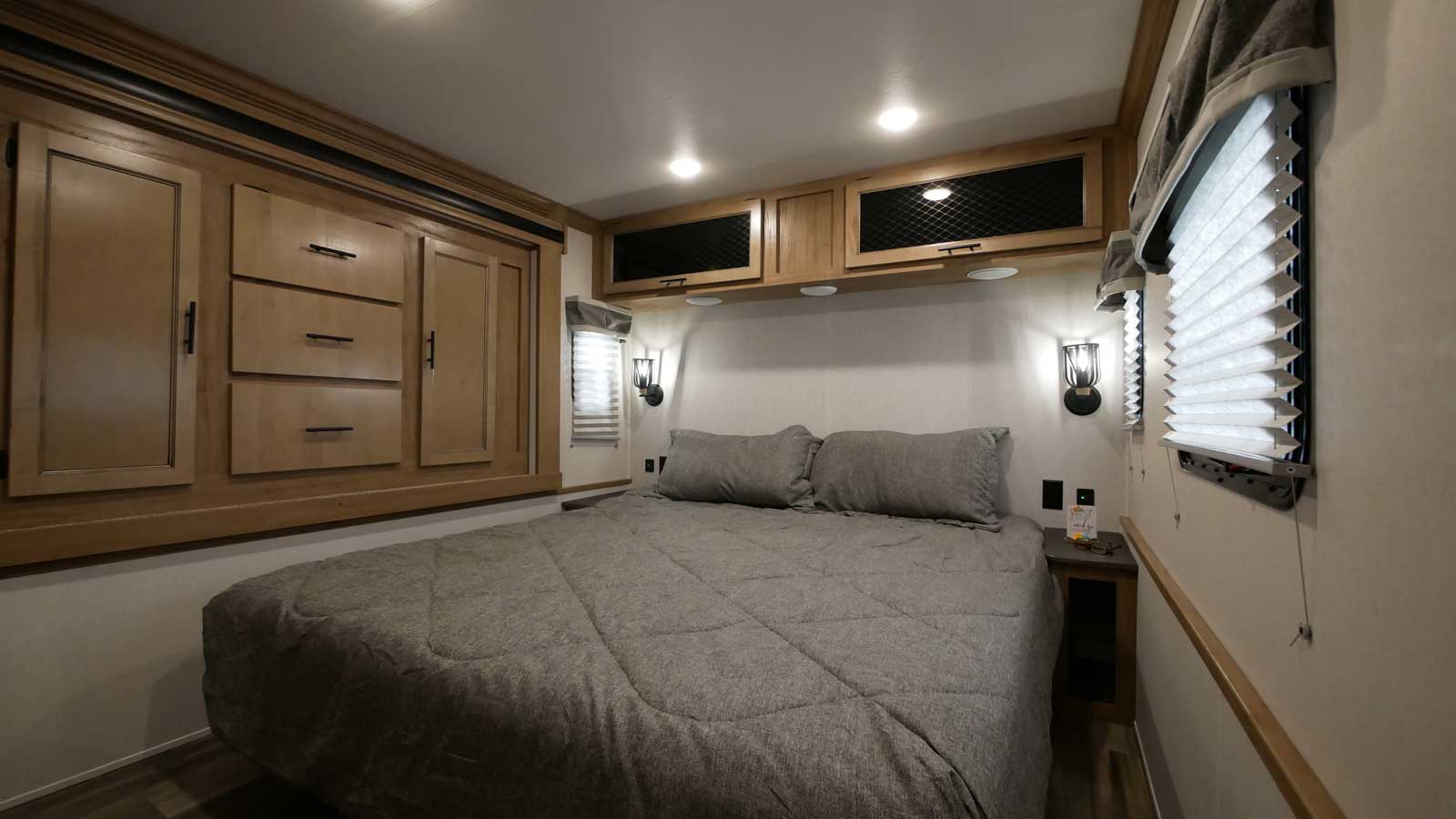 This RV rental bedroom features a comfy bed, built-in storage, wall lights, and blinds, offering a cozy interior.. Forest River Sabre 2021