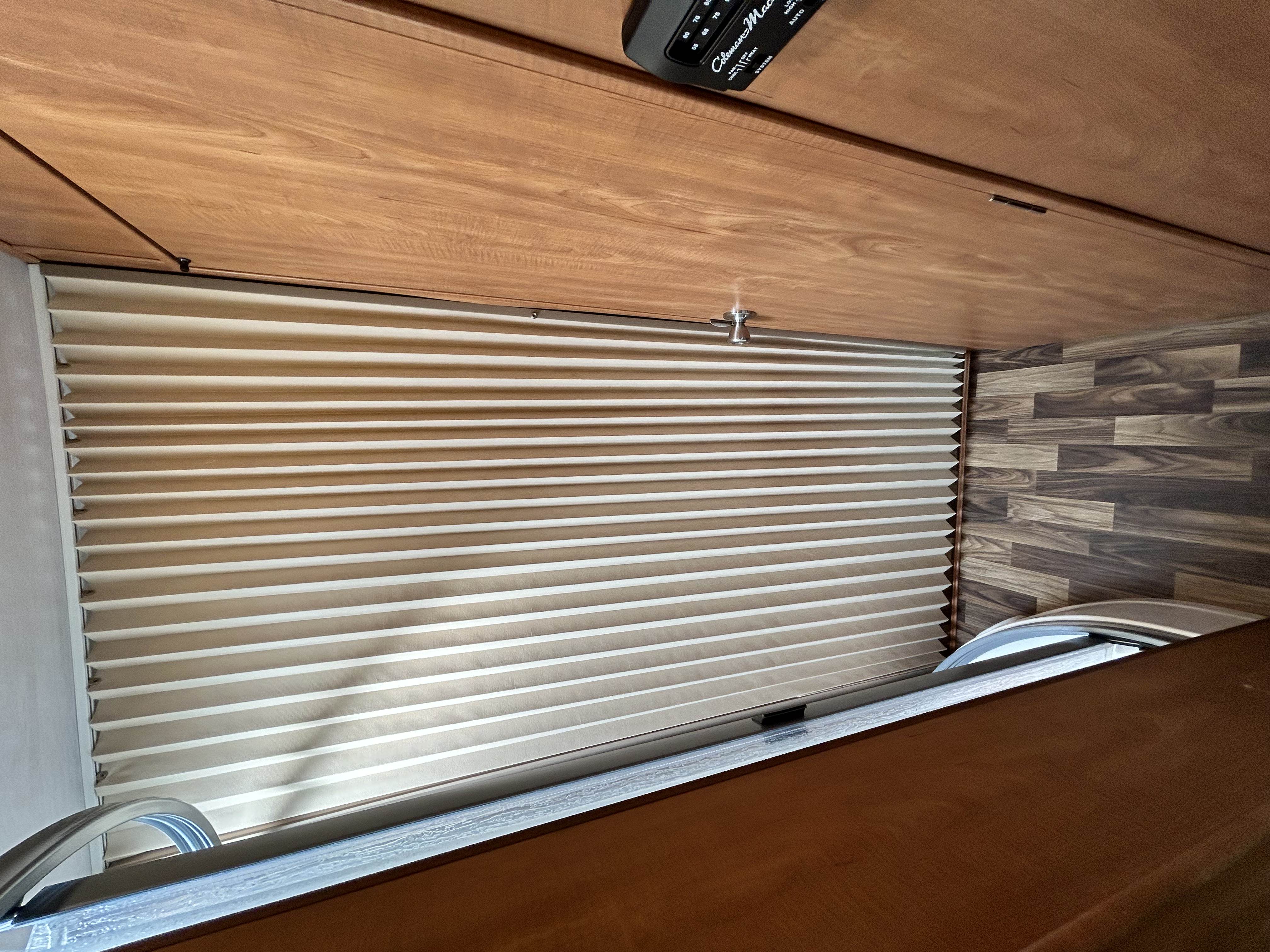 RV rental interior: closed pleated blinds, wooden wall paneling, and a Coleman-Mach climate control unit for comfort.. Nexus Phantom 2019