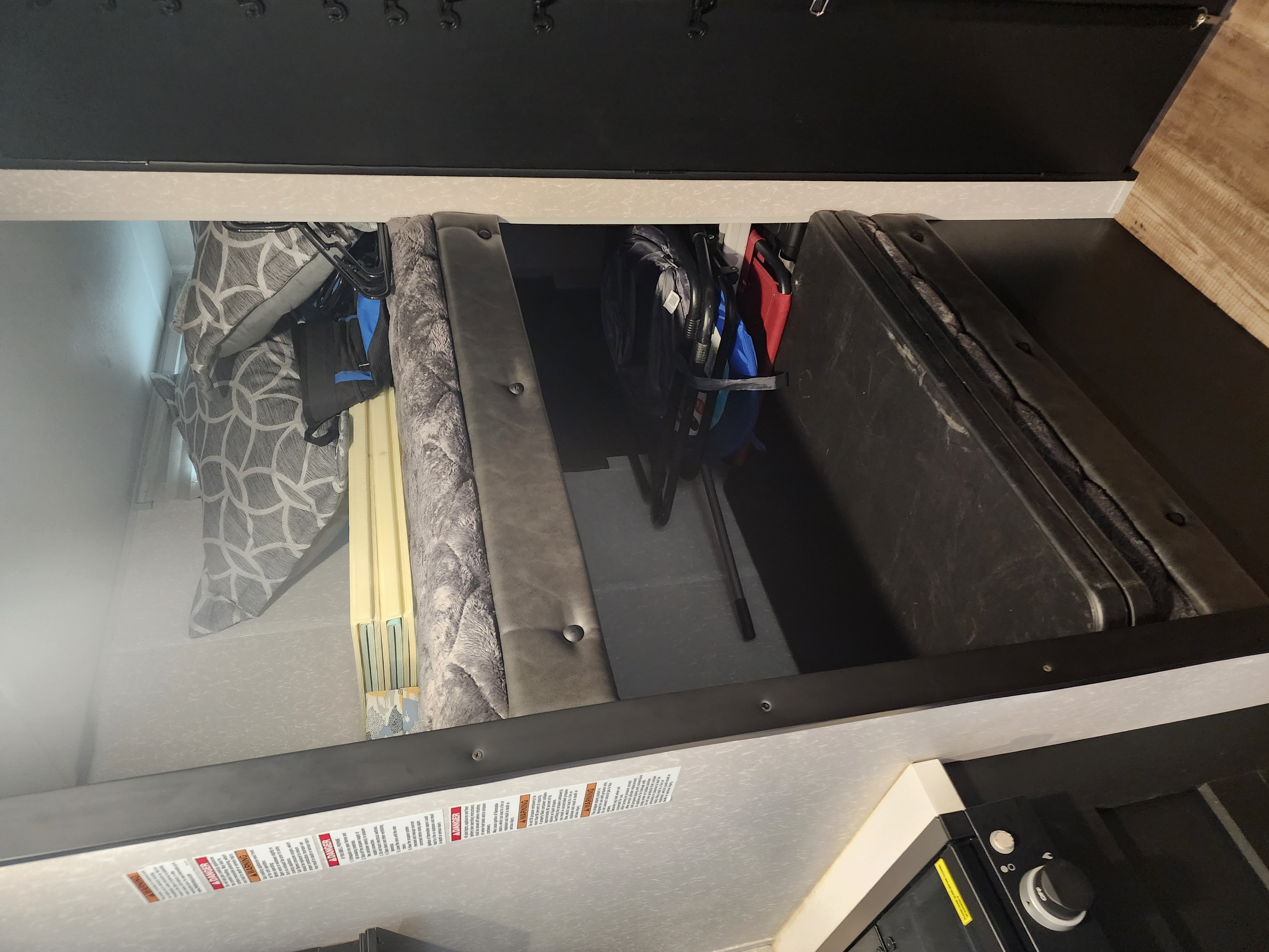 RV rental interior: A raised sleeping bunk with storage underneath, holding folded chairs, a table, and bedding for compact travel.. Forest River Cherokee Wolf Pup Black Label 2022