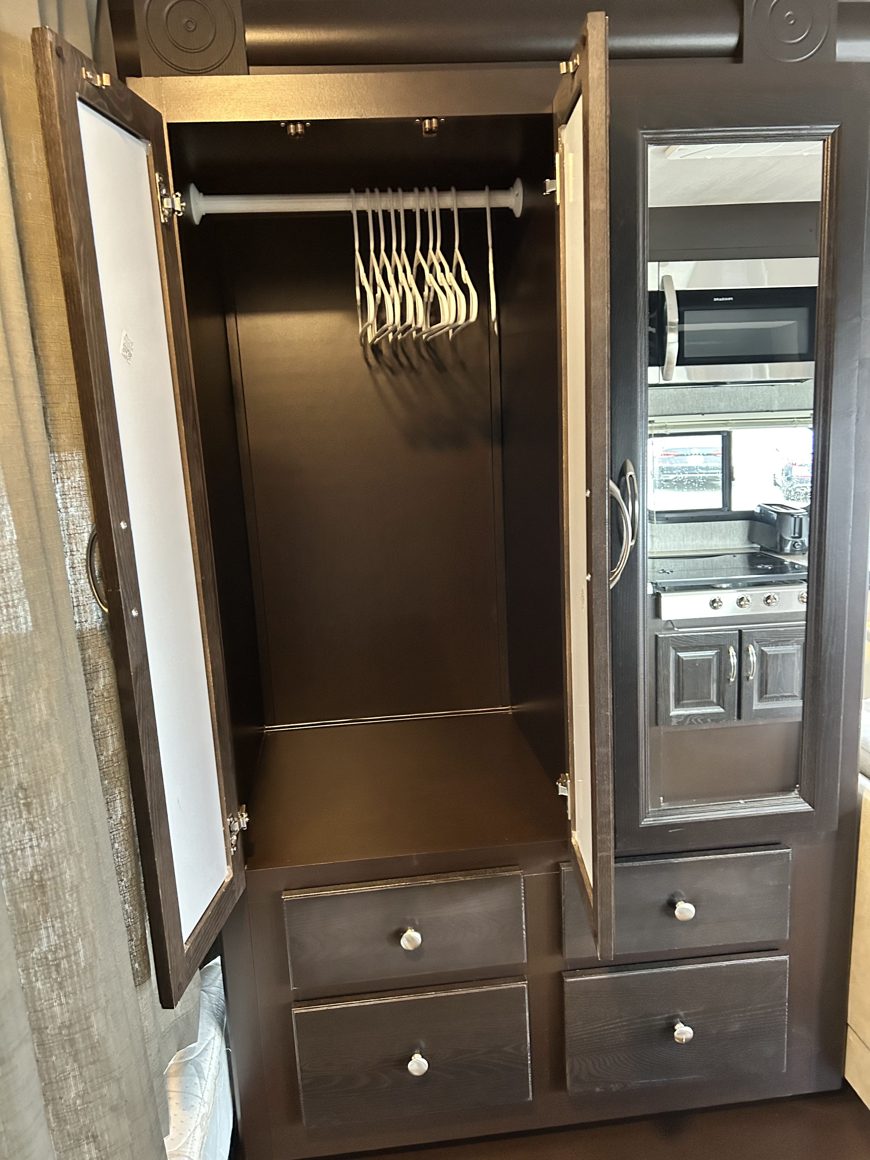 RV rental: Open wardrobe with hanging space, drawers. Mirrored door reflects a kitchen with microwave, stove, and window.. Nexus Phantom 2019