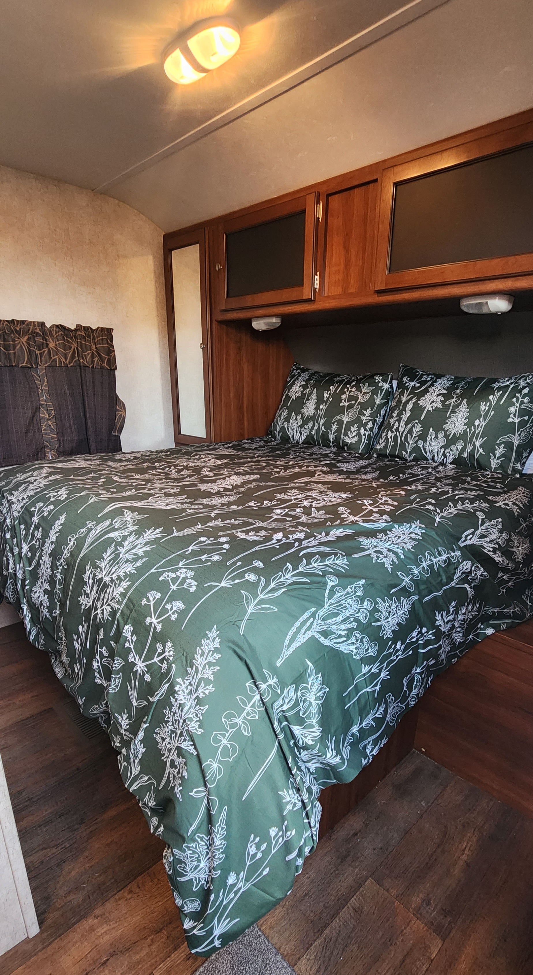 Comfortable RV rental bedroom with floral bedding, overhead storage, and warm lighting, perfect for a cozy stay.. Keystone RV Bullet Ultra Lite 2015