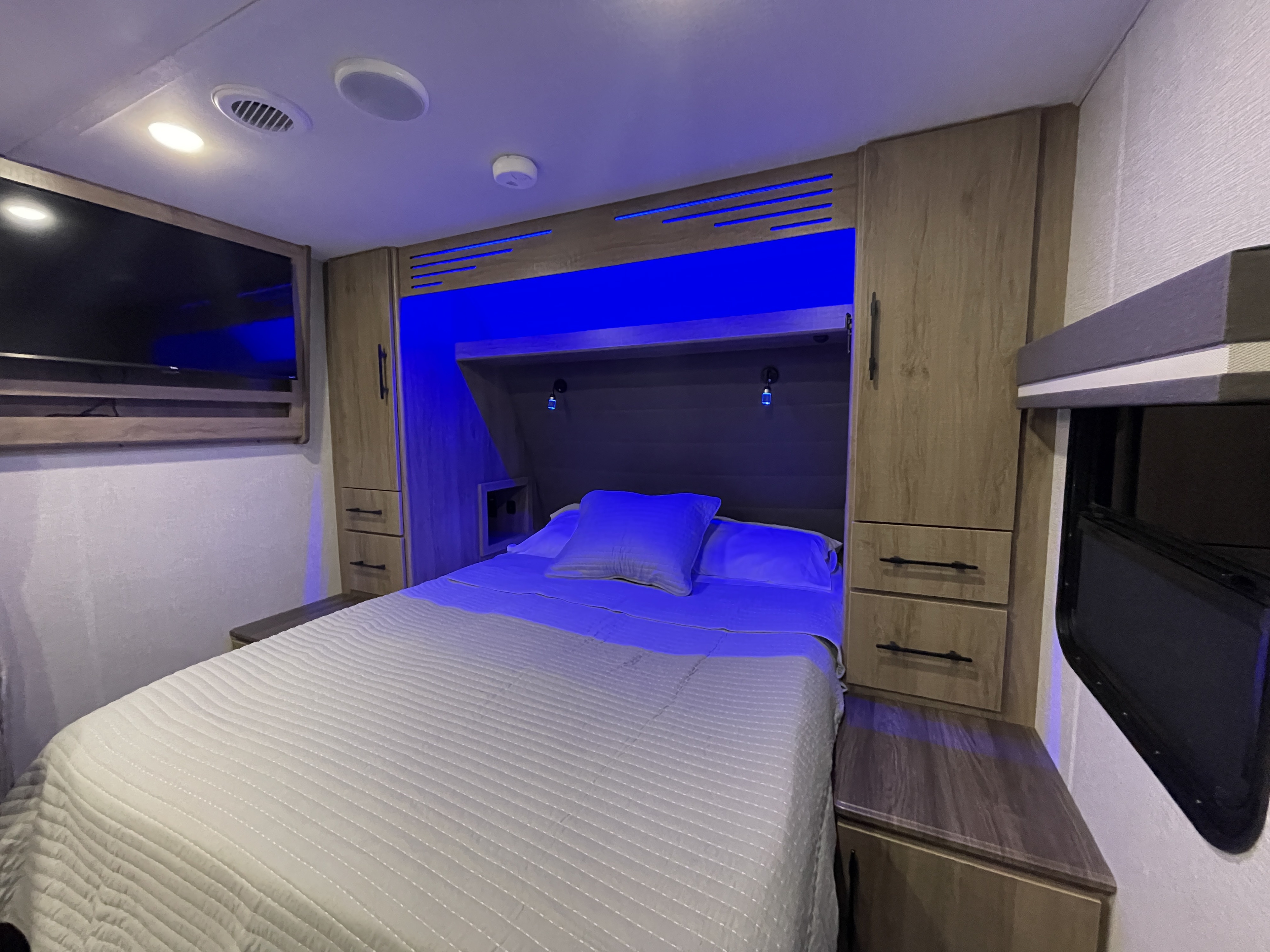 Cozy RV rental bedroom with modern blue lighting, comfortable bed, and wooden cabinetry. Perfect for your next adventure.. Grand Design Imagine XLS 2023