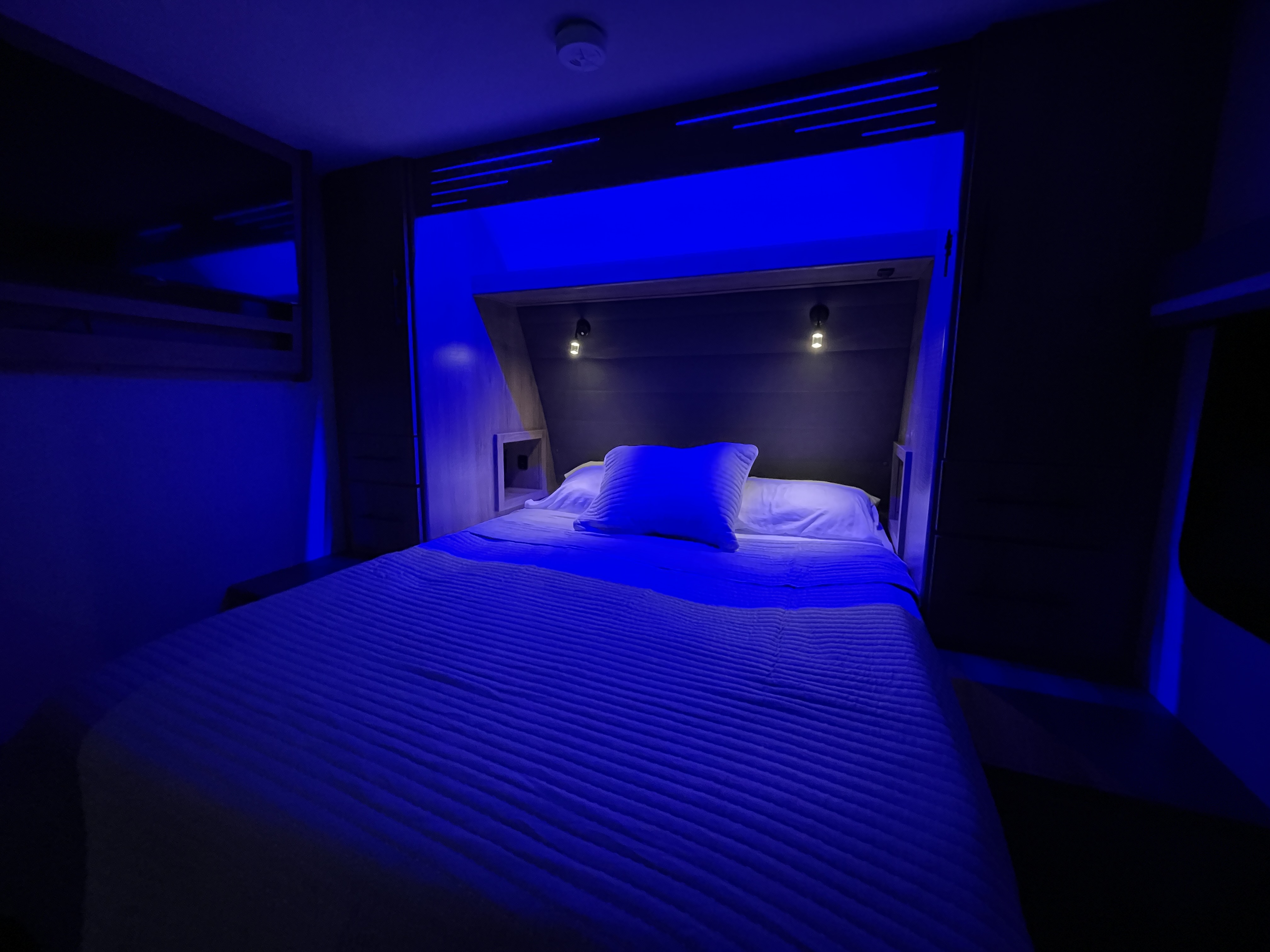 Relax in this RV rental bedroom with vibrant blue LED lighting. Features a comfortable bed, built-in storage, and reading lamps.. Grand Design Imagine XLS 2023