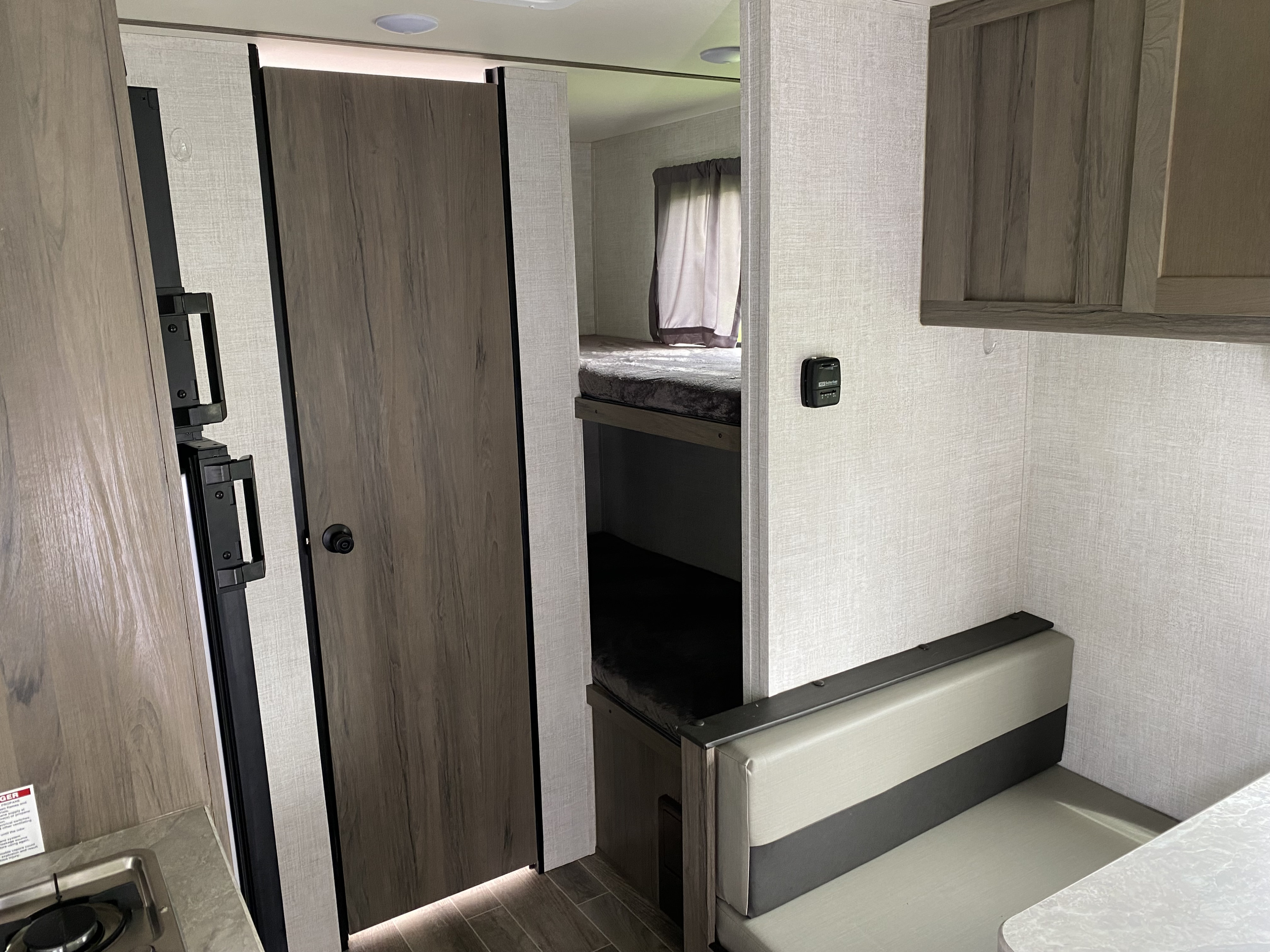 View inside an RV rental, showing grey bunk beds and a dinette with two-tone grey seating, next to a compact kitchen. A home on wheels.. Gulf Stream Ameri-Lite Super Lite 2021