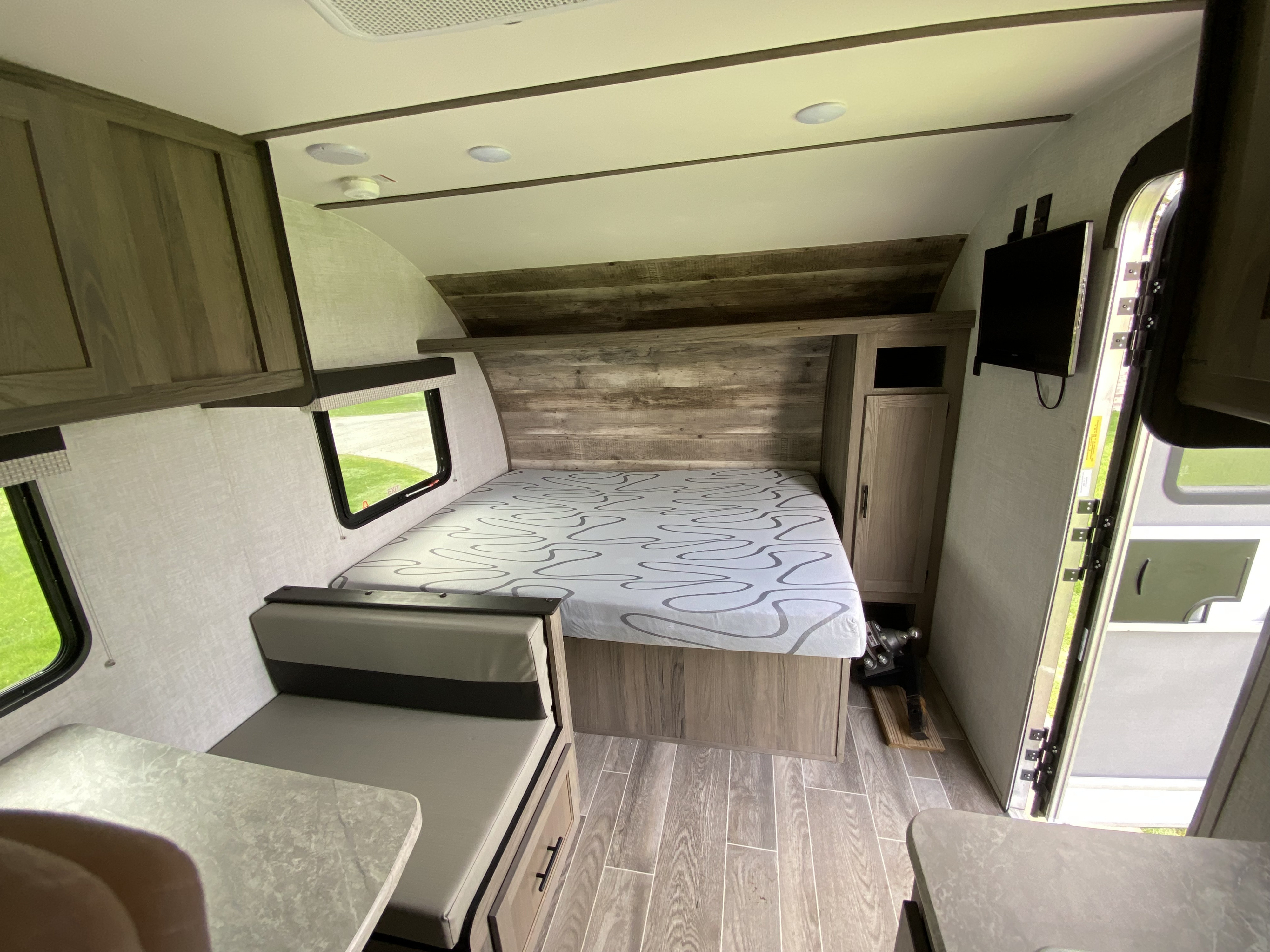 Inside a cozy RV rental: a modern living space with a patterned bed, a dinette, wood-look finishes, and overhead storage.. Gulf Stream Ameri-Lite Super Lite 2021