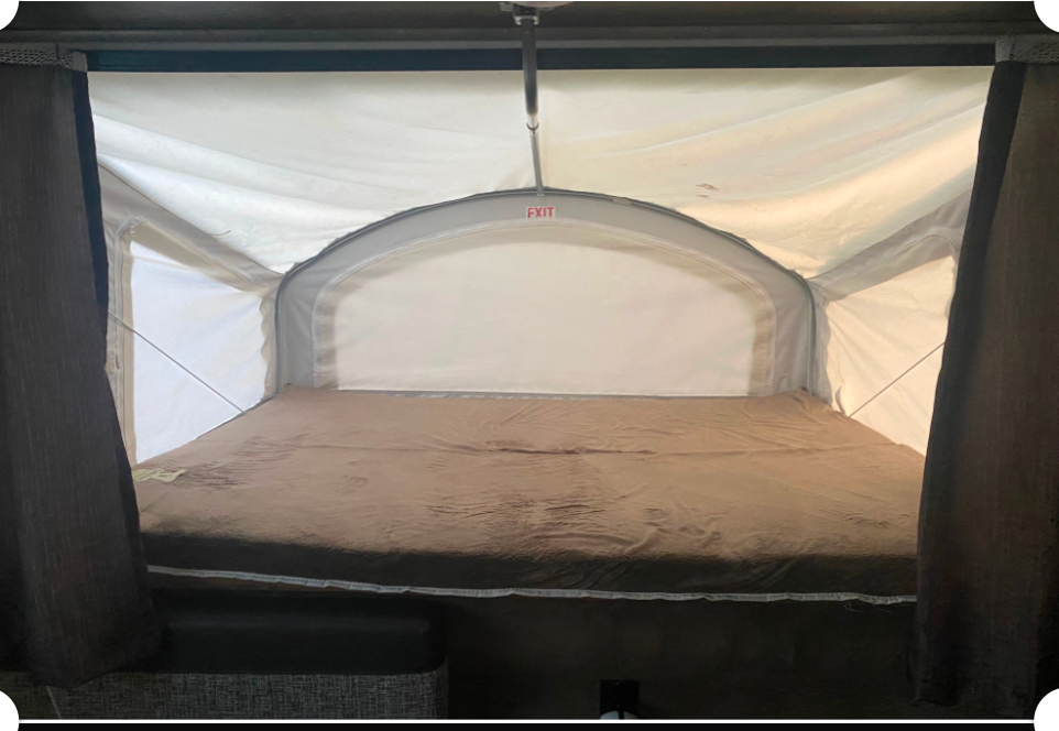 Inside a pop-up RV rental, a comfy bed is ready under canvas walls and an EXIT sign.. KZ Sportsman classic 2019
