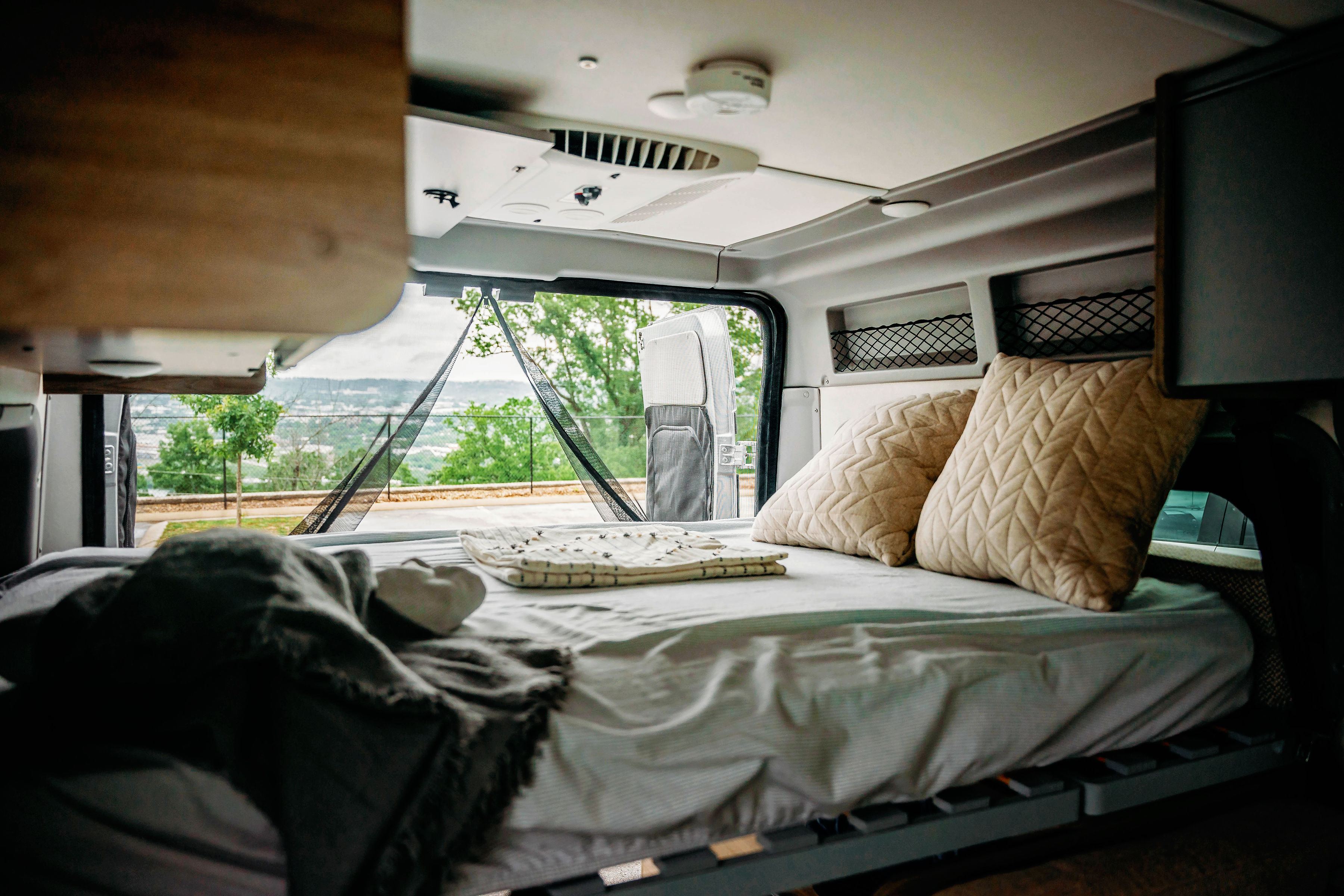 Cozy RV rental bedroom inside a camper van, showing a comfortable bed with a view through the screened back doors.. Winnebago Solis Pocket 2022