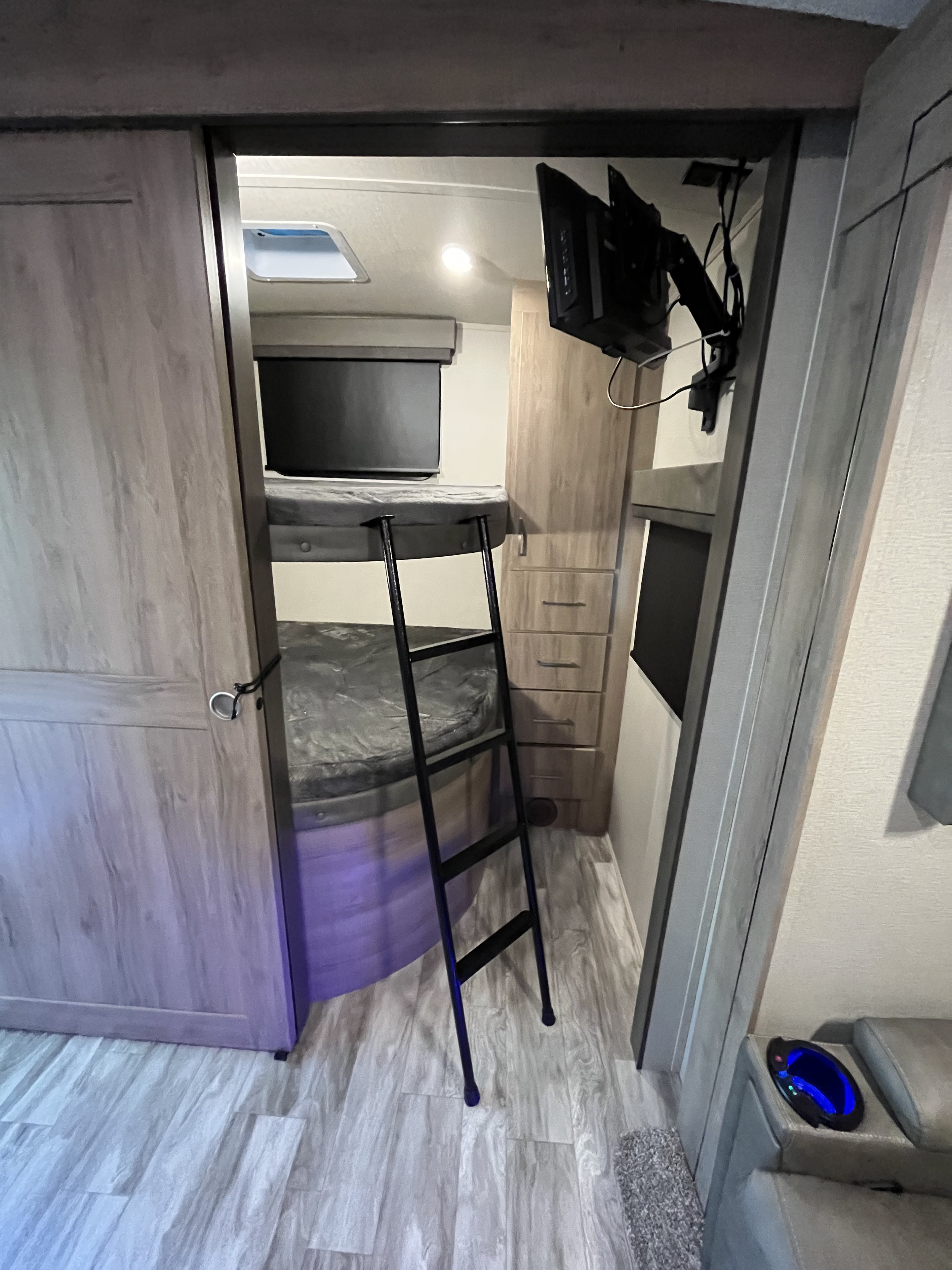 RV rental interior featuring comfortable bunk beds with a ladder, wall-mounted TV, and storage space.. Grand Design Imagine 2022