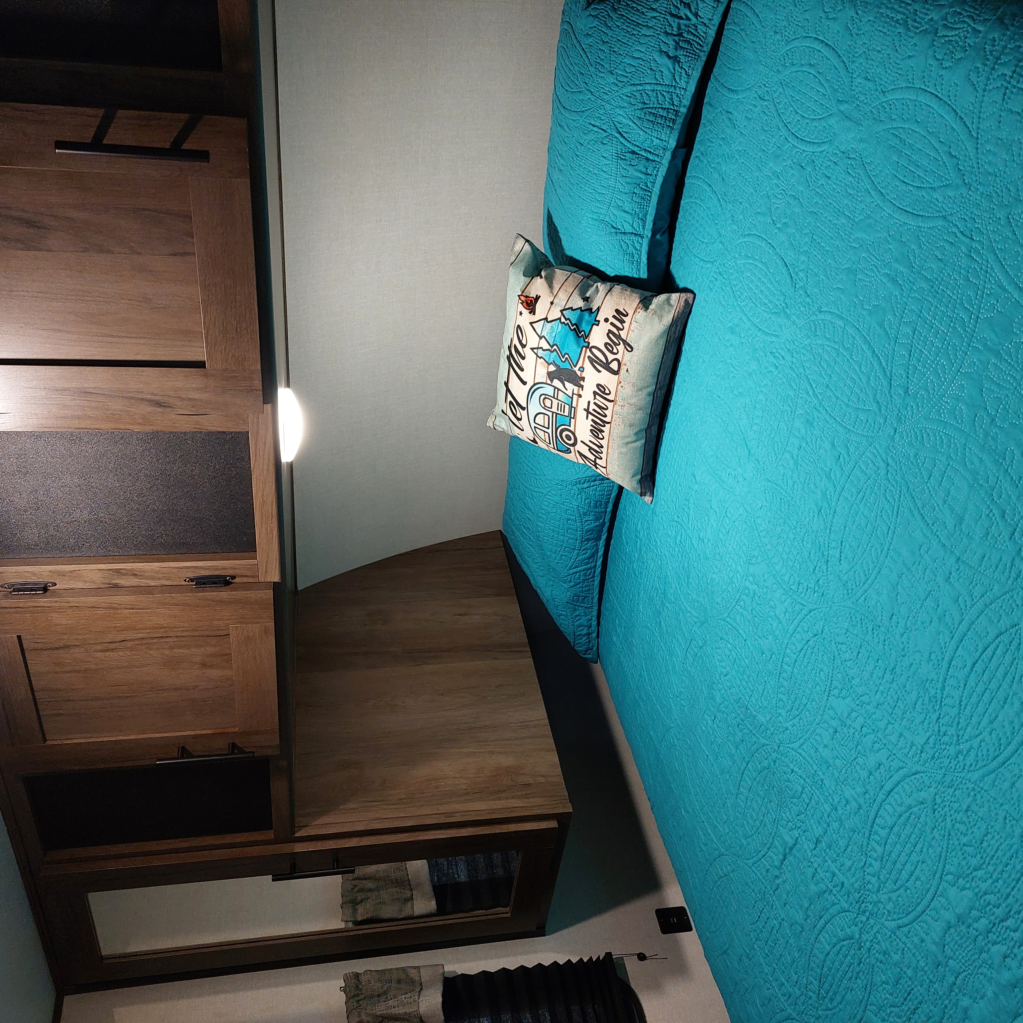 Experience comfort in this RV rental bedroom with a teal quilted bed, "Adventure Begin" pillow, and sleek wood cabinetry.. Avenger Avenger Trailer 2021