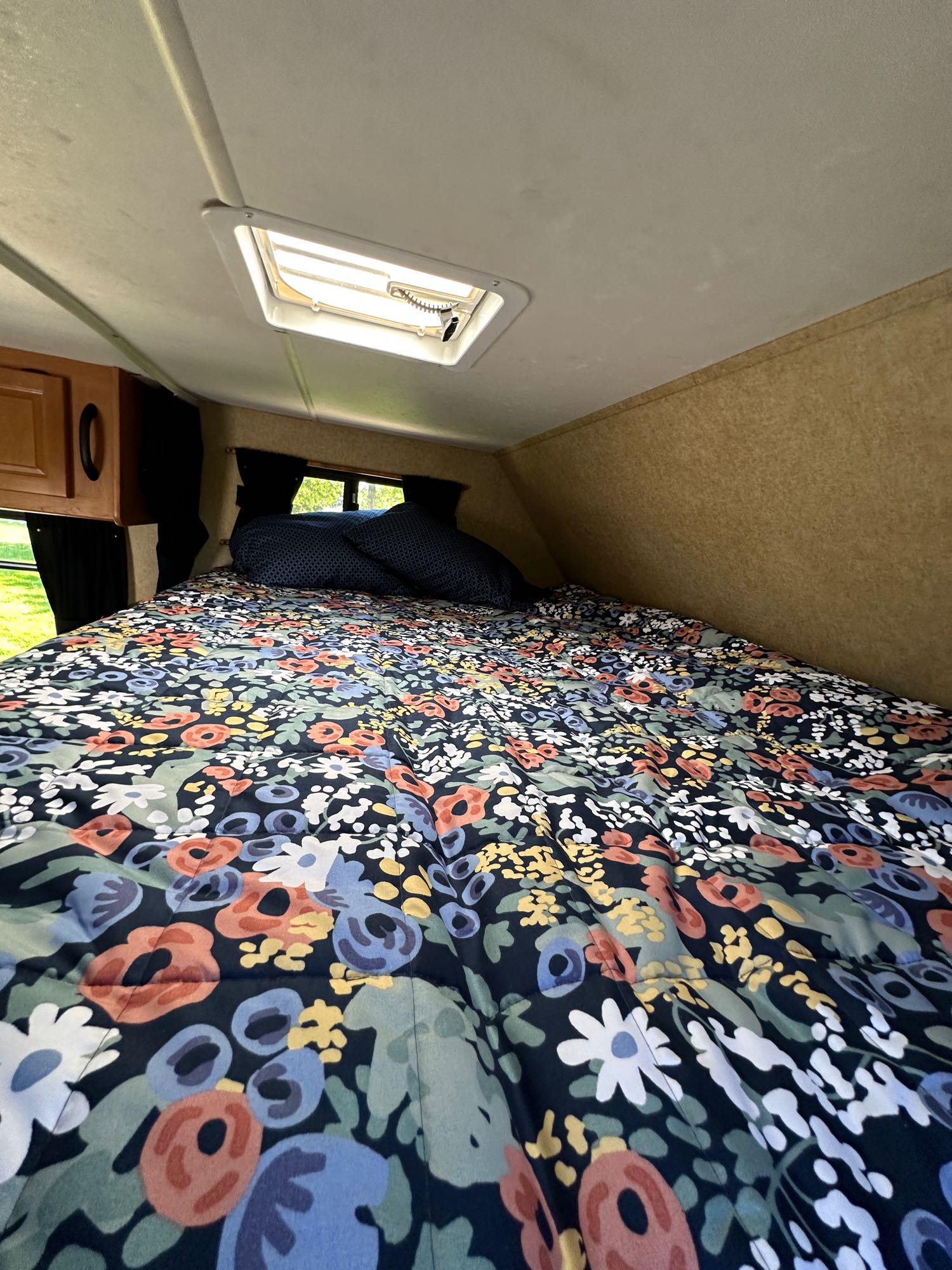 Cozy RV rental bedroom featuring a bed with a vibrant floral comforter, blue pillows, and an overhead skylight.. Thor Motor Coach Four Winds Majestic 2015