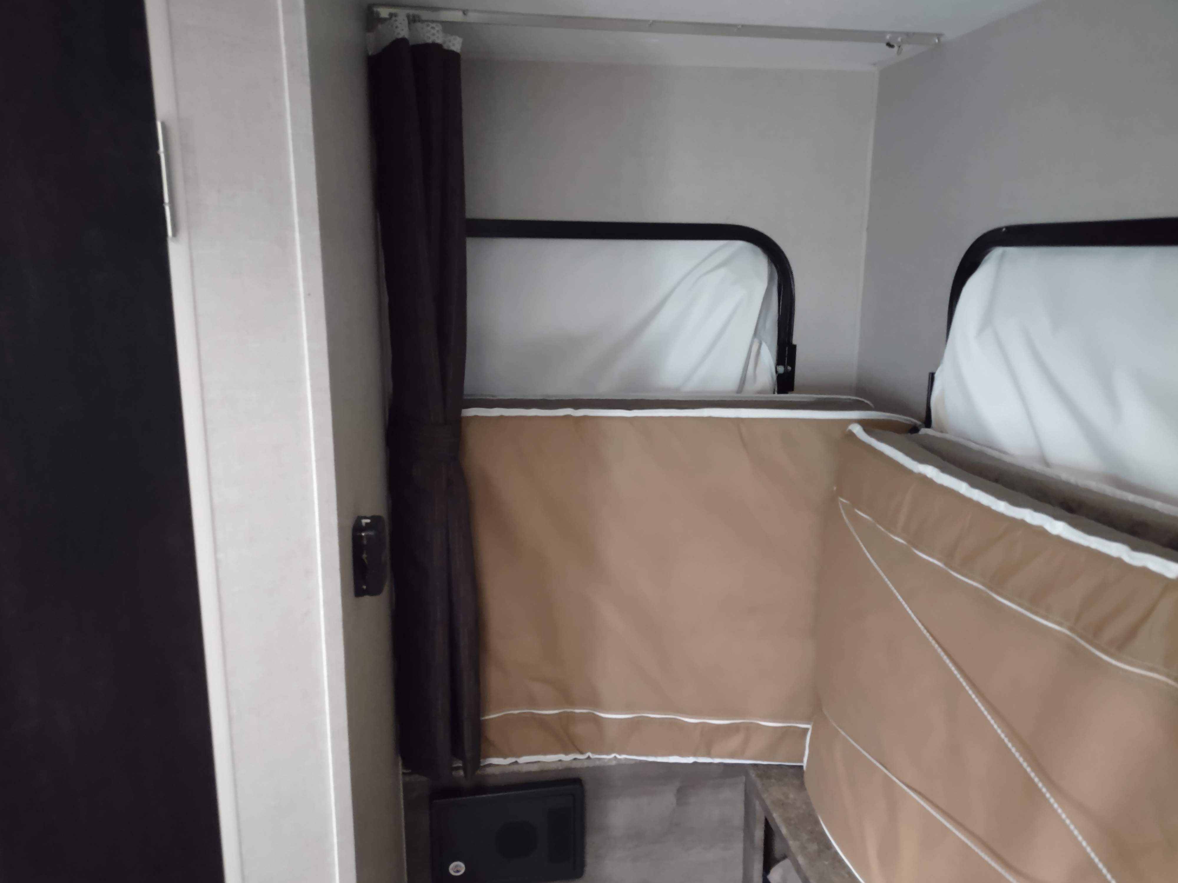 Inside an RV rental: Compact sleeping area with two bunk beds, brown fabric sides, white bedding, and a privacy curtain.. KZ Sportsman classic 2019