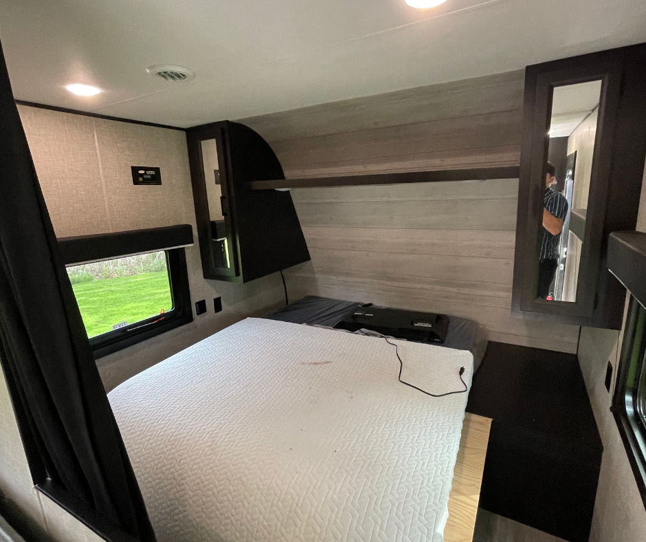 Cozy RV rental bedroom featuring a white mattress, window view of green grass, and dark built-in cabinetry.. Jayco Jay Flight SLX 2022