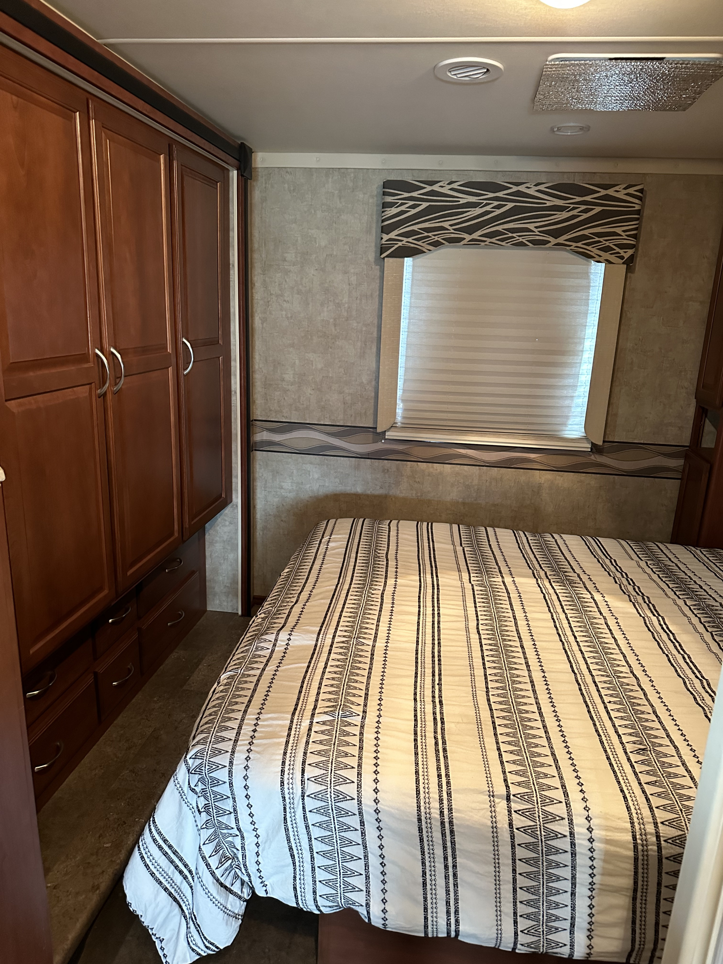 RV rental bedroom showcasing a cozy bed with patterned linens, wooden cabinets, and a window with blinds.. Winnebago Minnie Winnie 2015