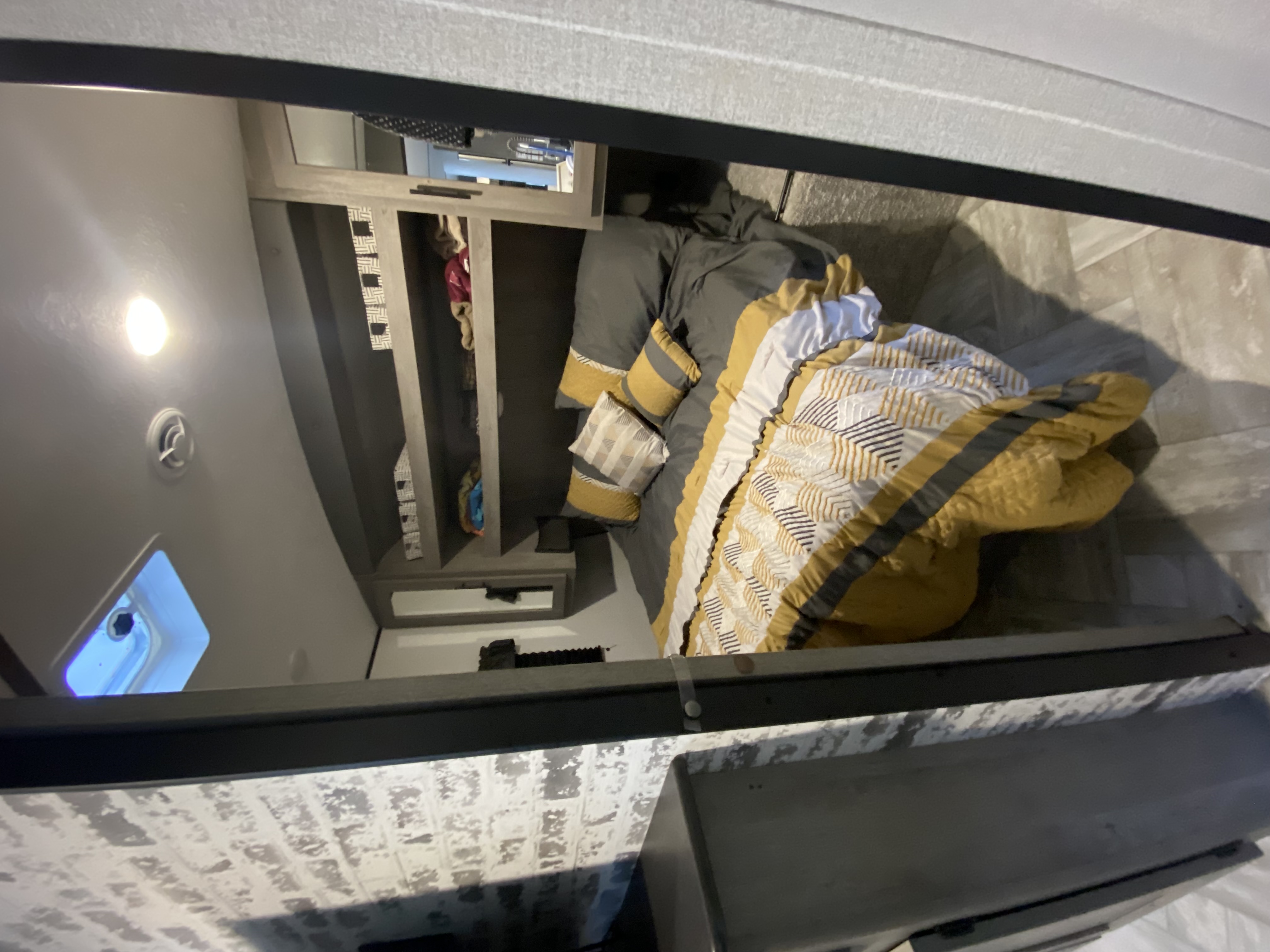 Cozy RV rental bedroom featuring gray and yellow bedding, built-in shelving, and a light-colored floor.. Keystone RV Springdale 2021