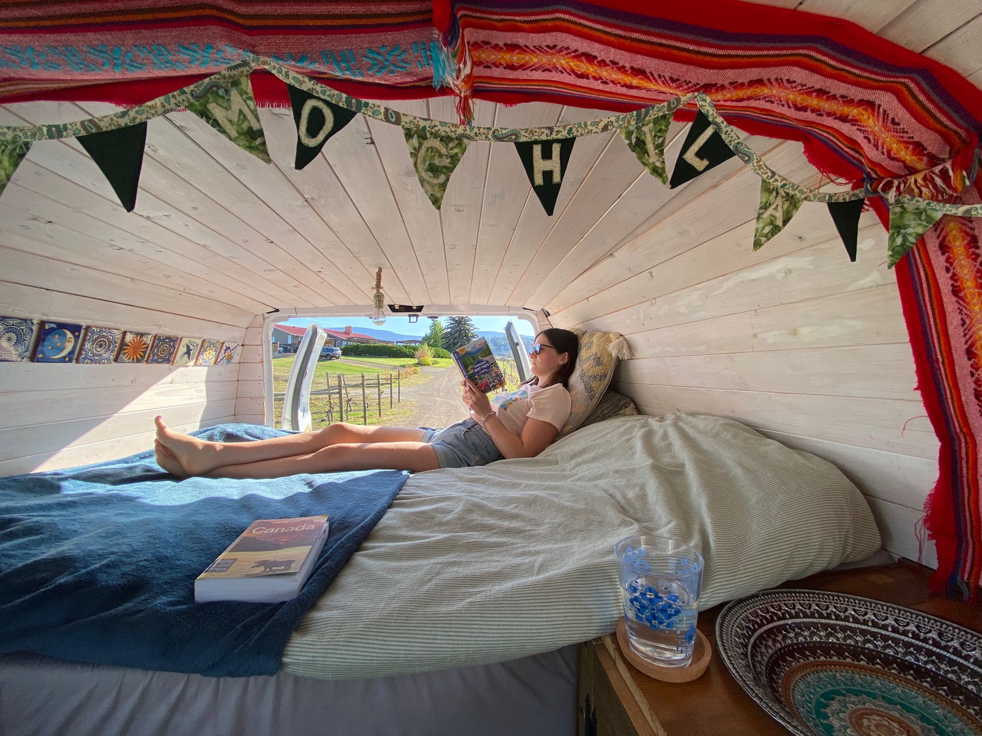 Enjoy a cozy rv rental! A person reads in a custom van with an "OH CANADA" banner, perfect for travel & relaxation.. Ford Econoline 150 2009