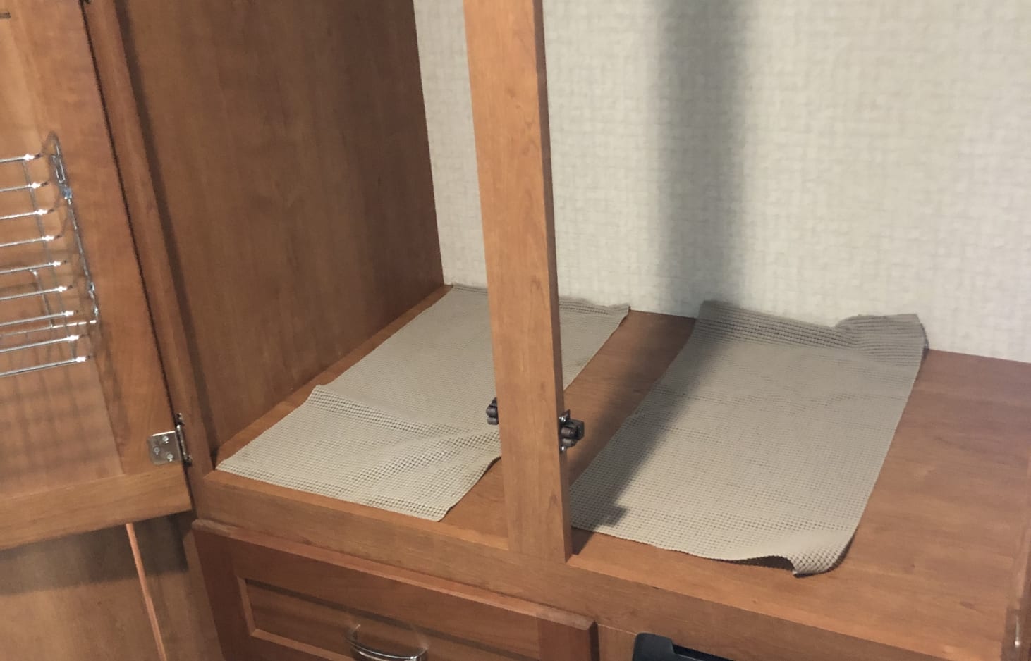 RV rental cabinet interior with anti-slip mats on wooden shelves and a door rack for organized storage.. Winnebago Minnie Winnie 2016