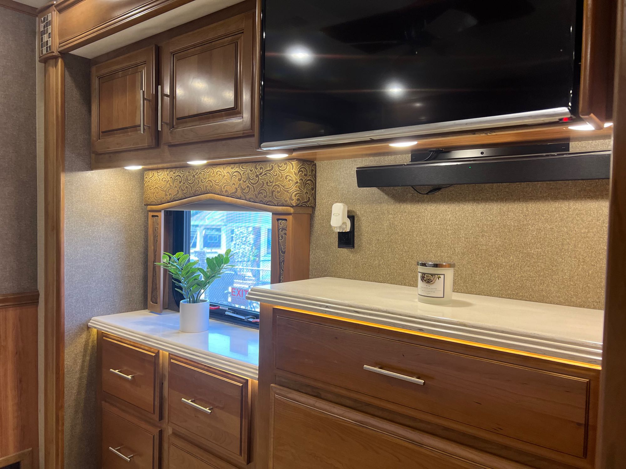 Explore the comfortable RV rental bedroom with warm lighting, wood cabinets, a TV, and storage for a cozy stay.. Entegra Coach Aspire 2018