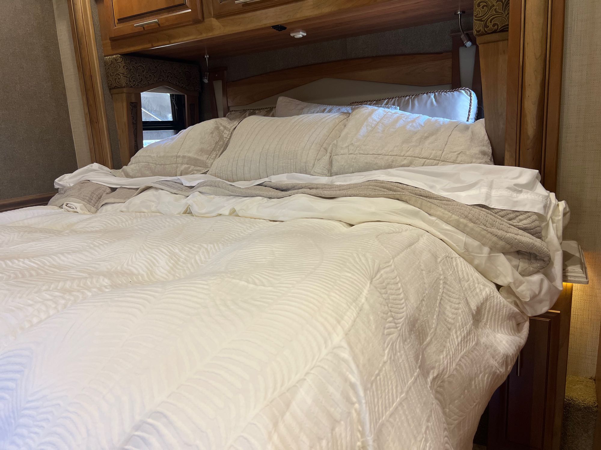 Cozy RV rental bedroom with a large, inviting bed, soft pillows, and a white patterned comforter, promising restful nights.. Entegra Coach Aspire 2018