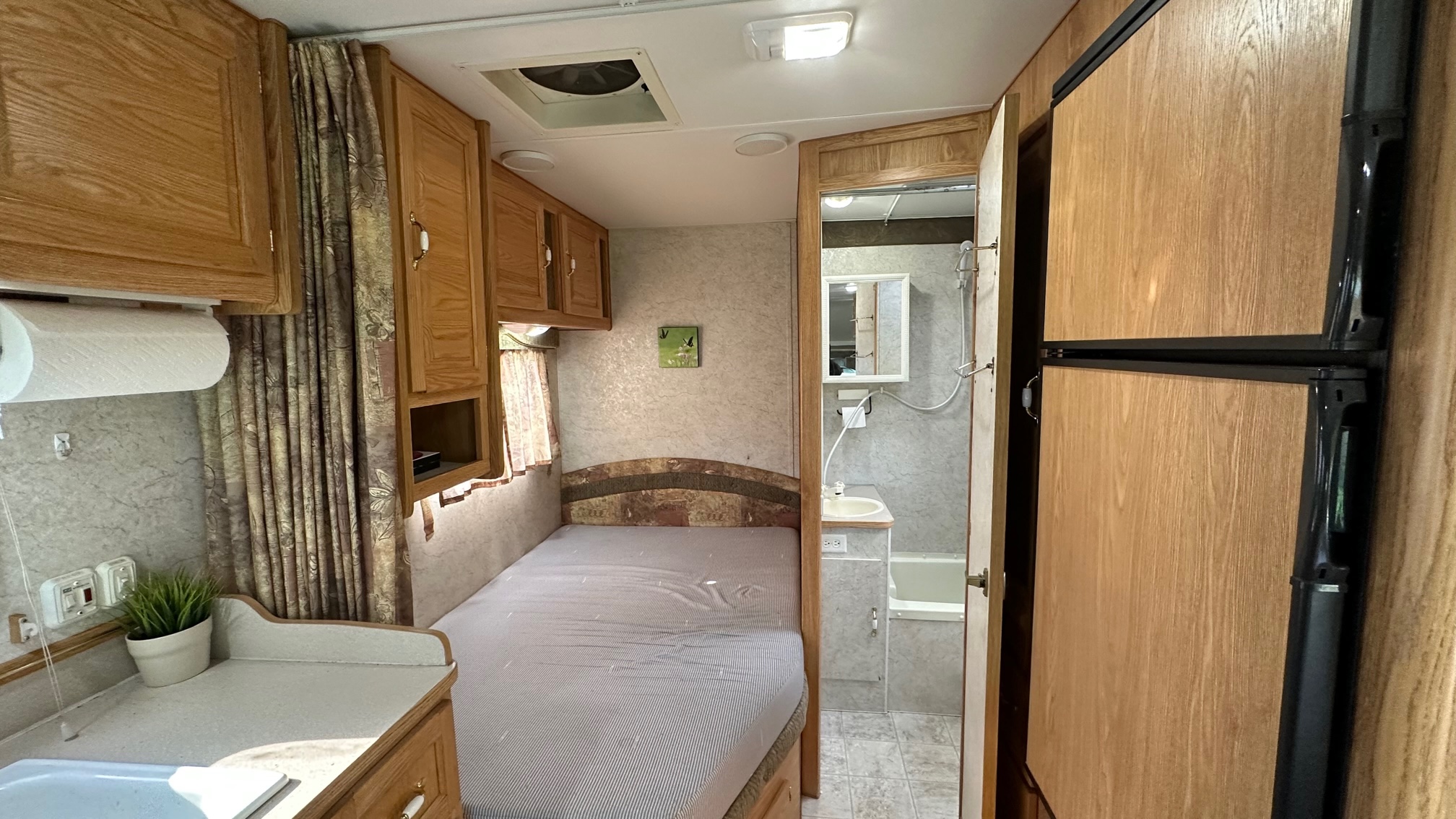 Inside this RV rental: wood cabinets, cozy bed, kitchenette with paper towels, and a compact bathroom. Fridge visible.. Adventurer Adventurer Motorhome 2005