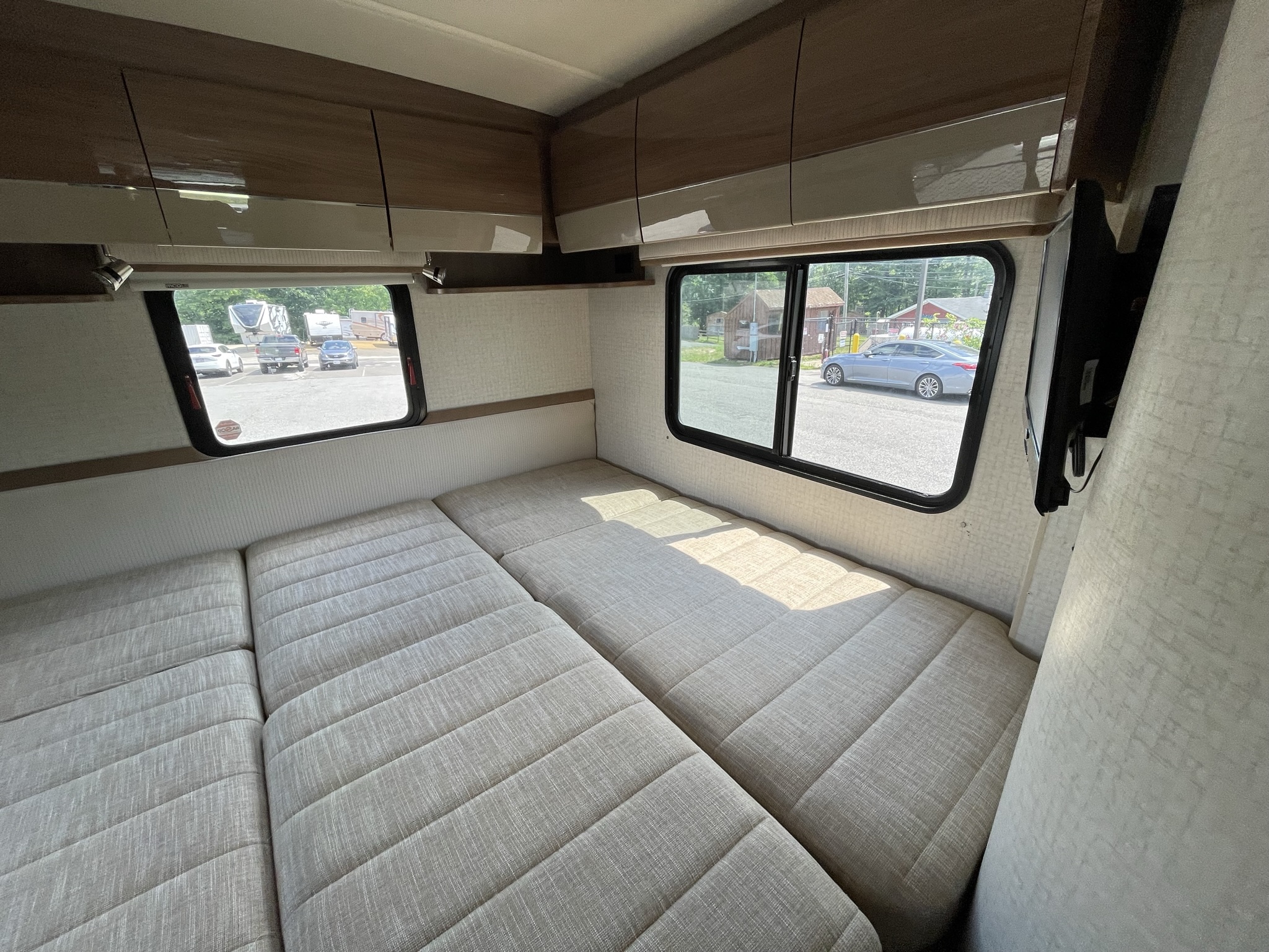 Inside an RV rental: a light-colored modular bed/seating area, sleek overhead cabinets, and large windows revealing the outside view.. Itasca Navion 2015