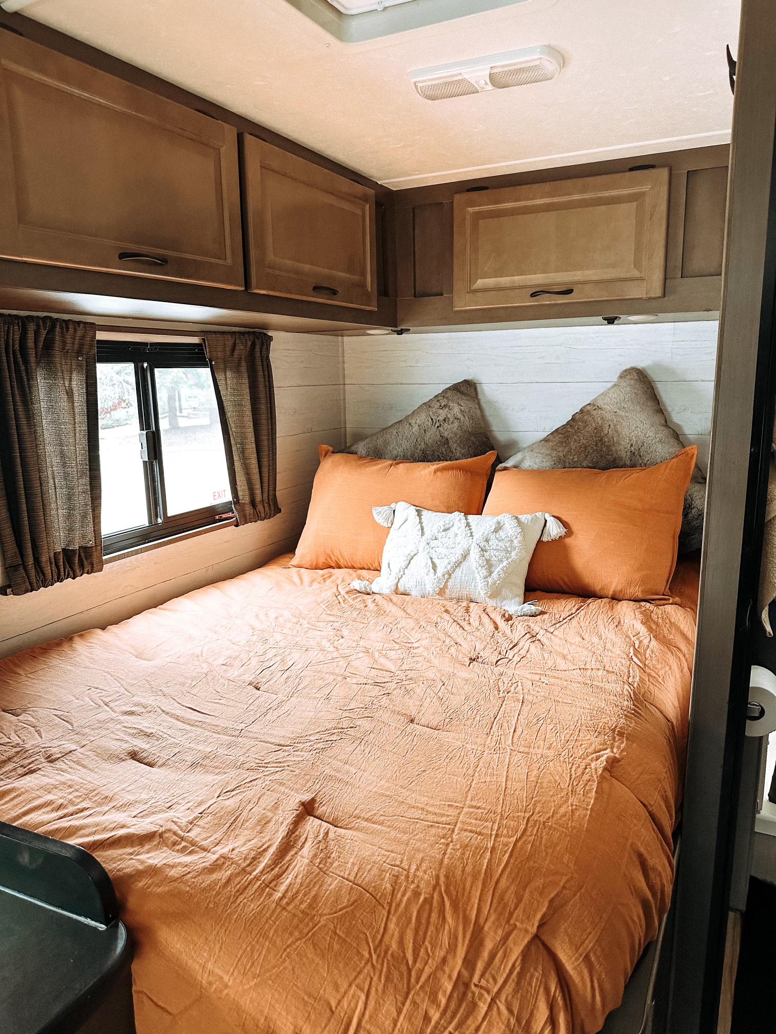 Cozy RV rental bedroom with an orange bed, fluffy pillows, wood cabinets, and a window offering a glimpse of nature. Perfect compact lodging.. Thor Majestic 2019