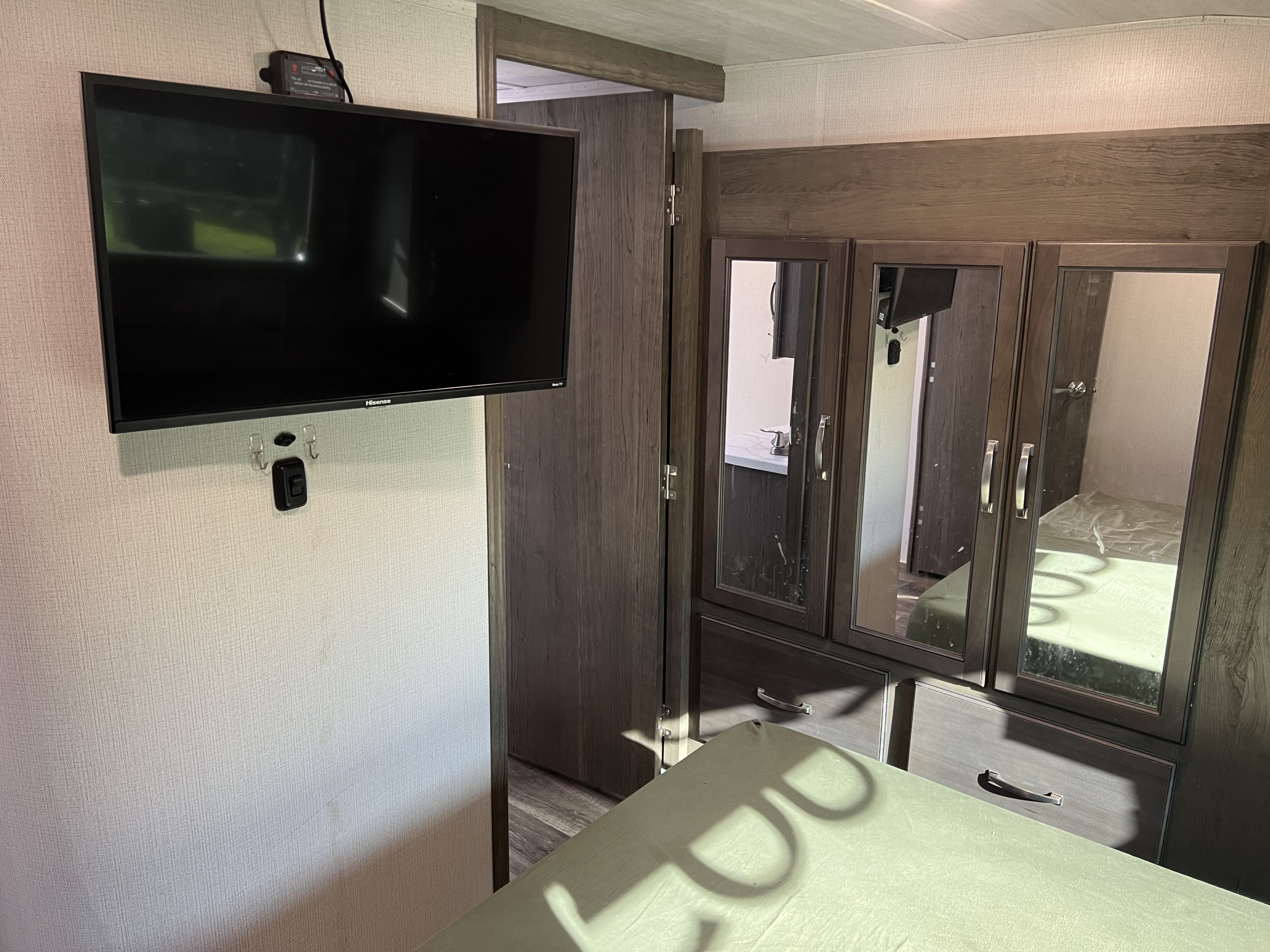 An RV rental bedroom showcasing a wall-mounted TV, mirrored wardrobe, and part of the bed for a compact living space.. Keystone RV Cougar 364 BHL 2022