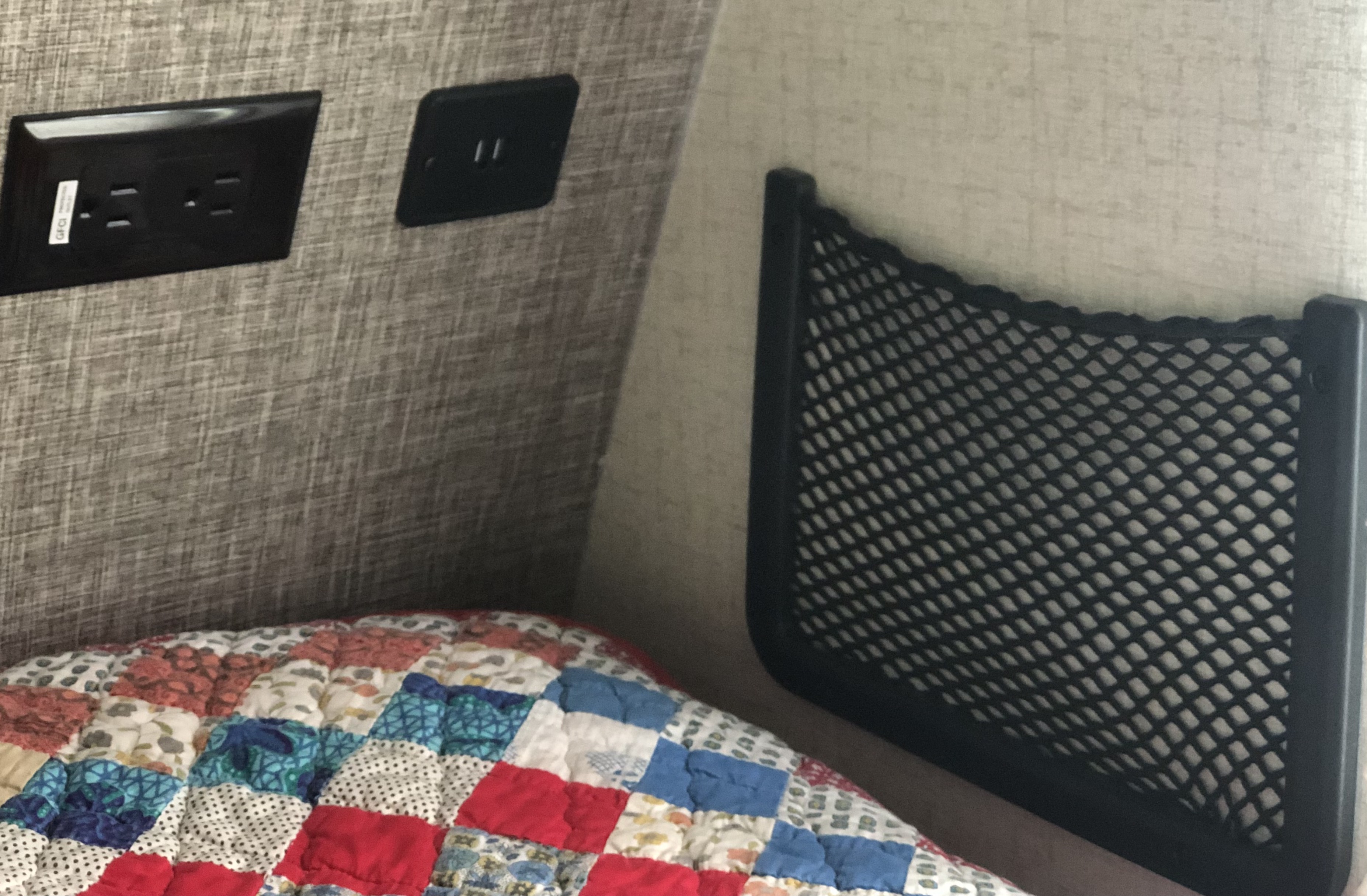 Cozy RV rental interior: GFCI outlet, USB port, and bedside storage net above a colorful quilt.. Winnebago Micro Minnie Delivery Only 2022