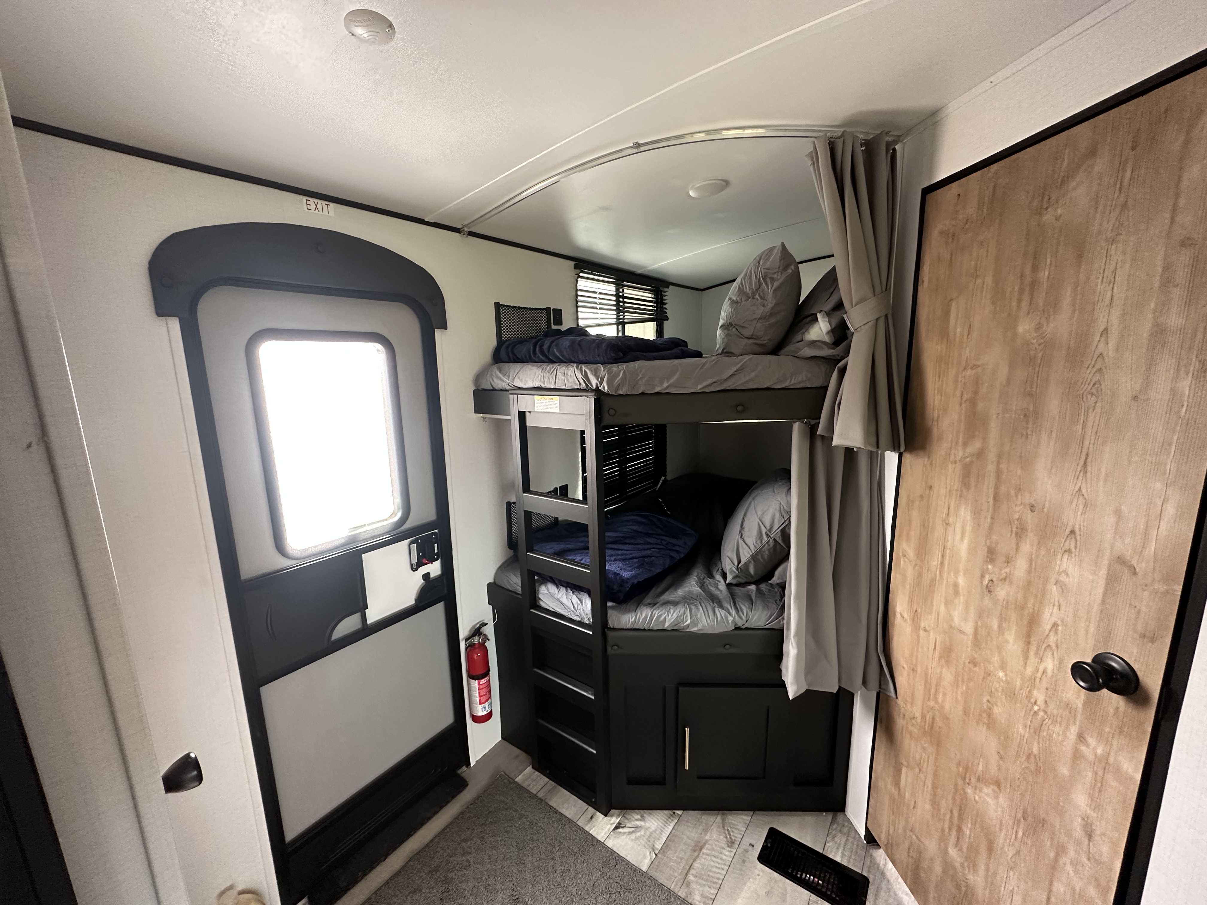 Cozy RV rental interior: bunk beds, main entrance with fire extinguisher, & a private wood-look door for comfort.. Keystone RV Springdale 2022