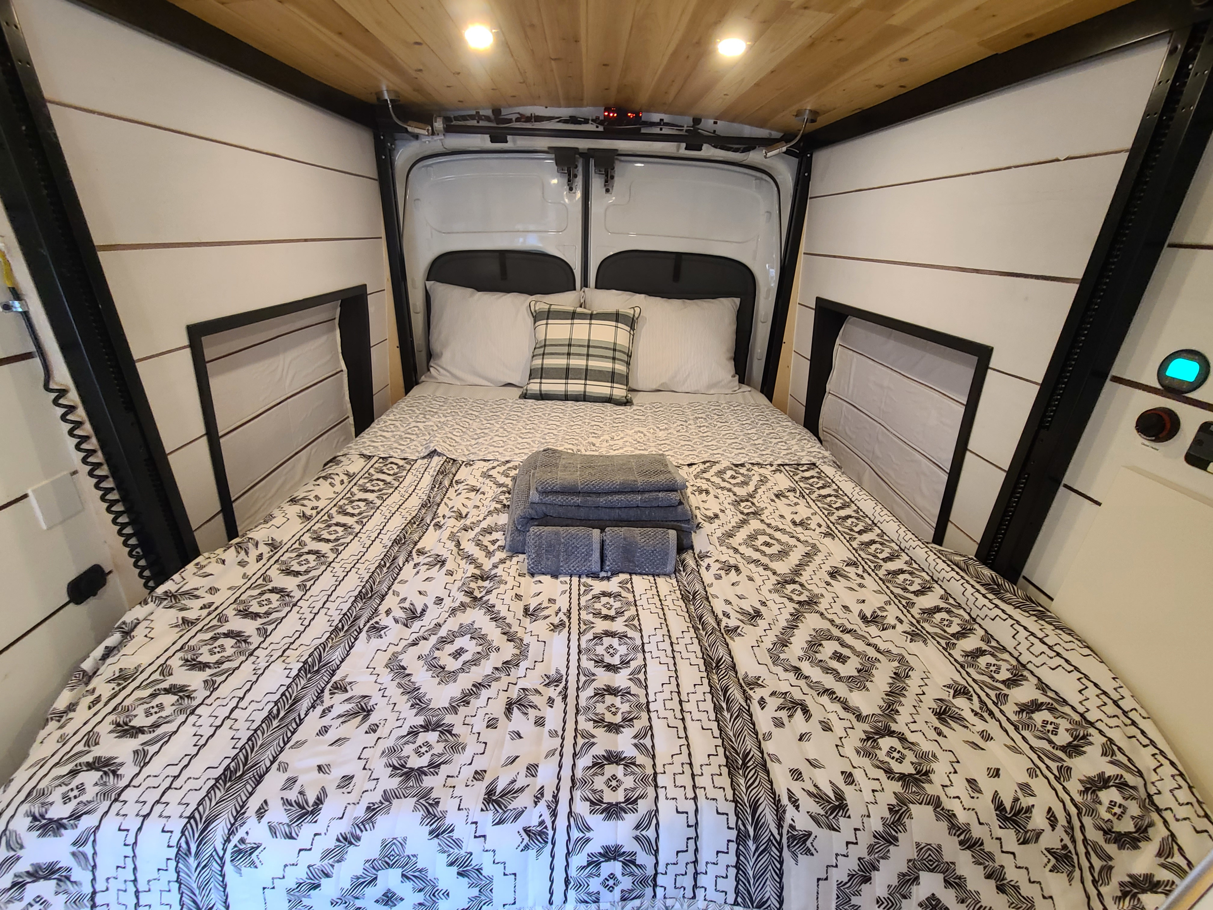Cozy RV rental sleeping area: Bed with patterned black/white bedding, pillows, fresh towels, wood ceiling, & warm lighting.. Other Other 2016