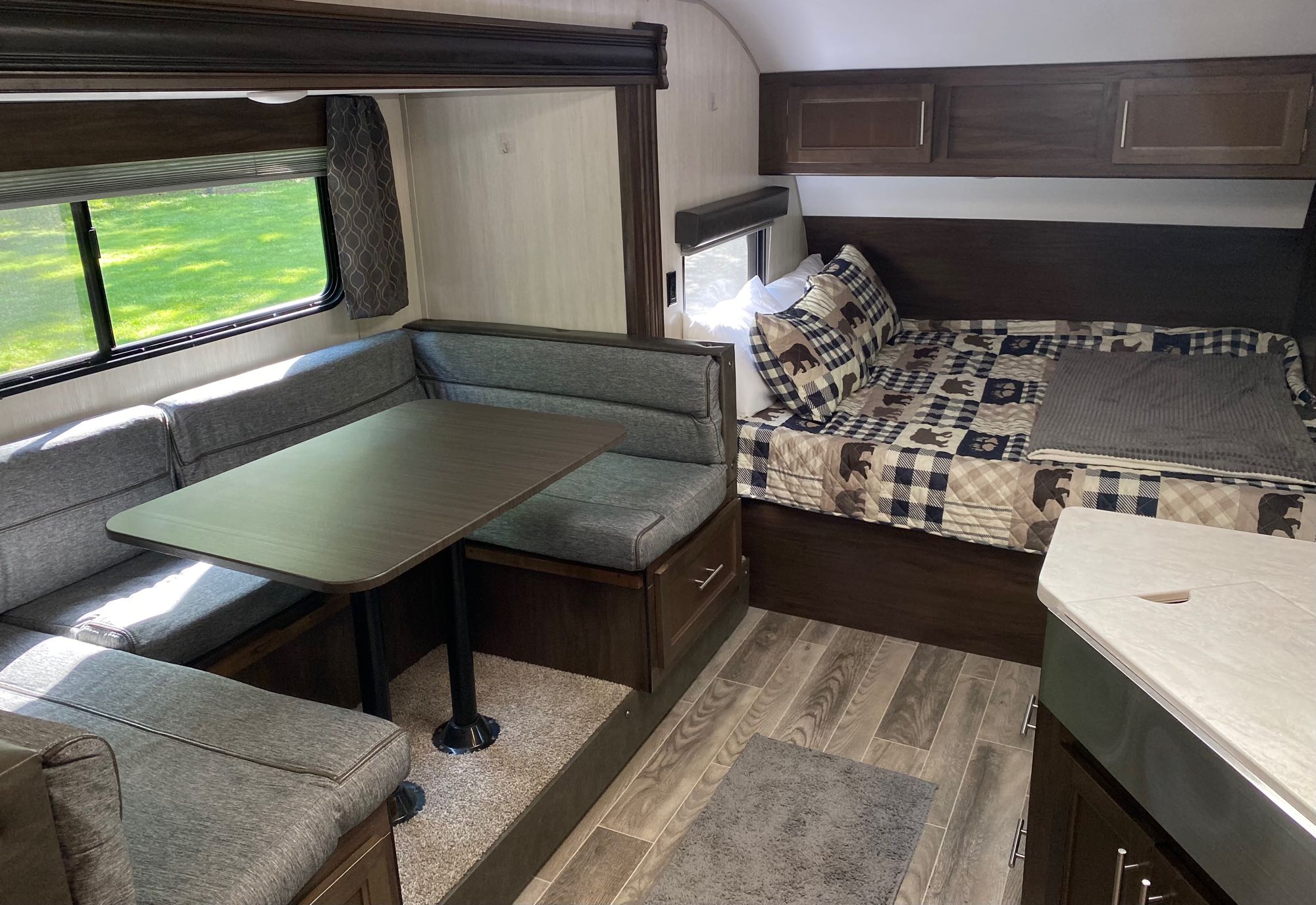 Cozy RV rental interior with a grey dinette, plaid bear-themed bed, and overhead storage.. Forest River Cherokee Grey Wolf 2019