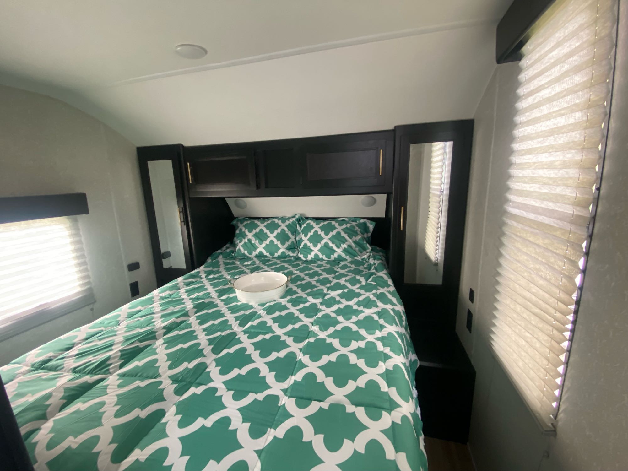 Cozy RV rental bedroom features a comfy bed with vibrant green bedding, overhead cabinets, and window blinds for privacy.. Forest River Cherokee Grey Wolf 2022