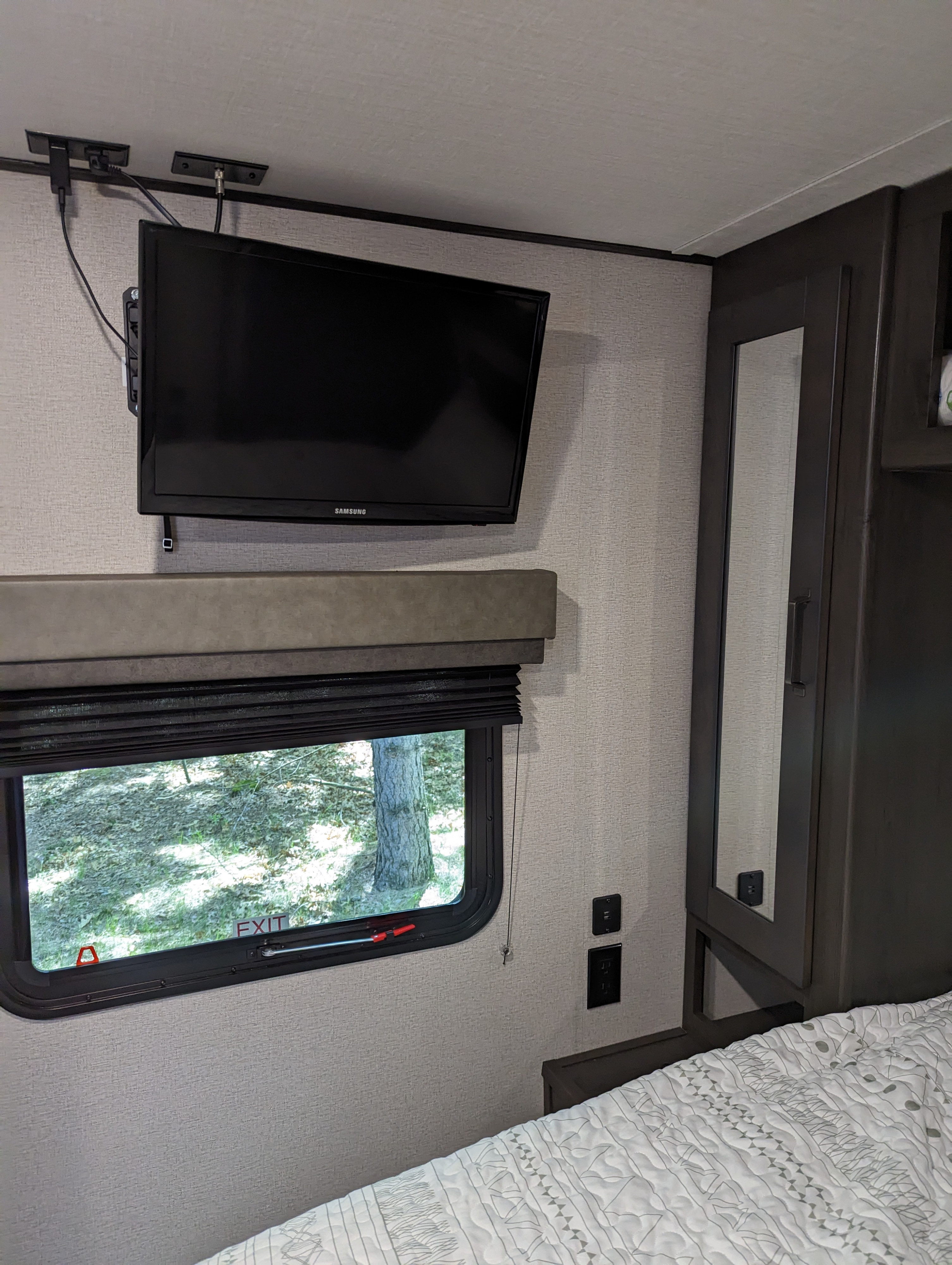 RV rental bedroom view: wall-mounted Samsung TV, window with blinds, and USB outlets beside a bed and wardrobe.. Grand Design Transcend Xplor 2022