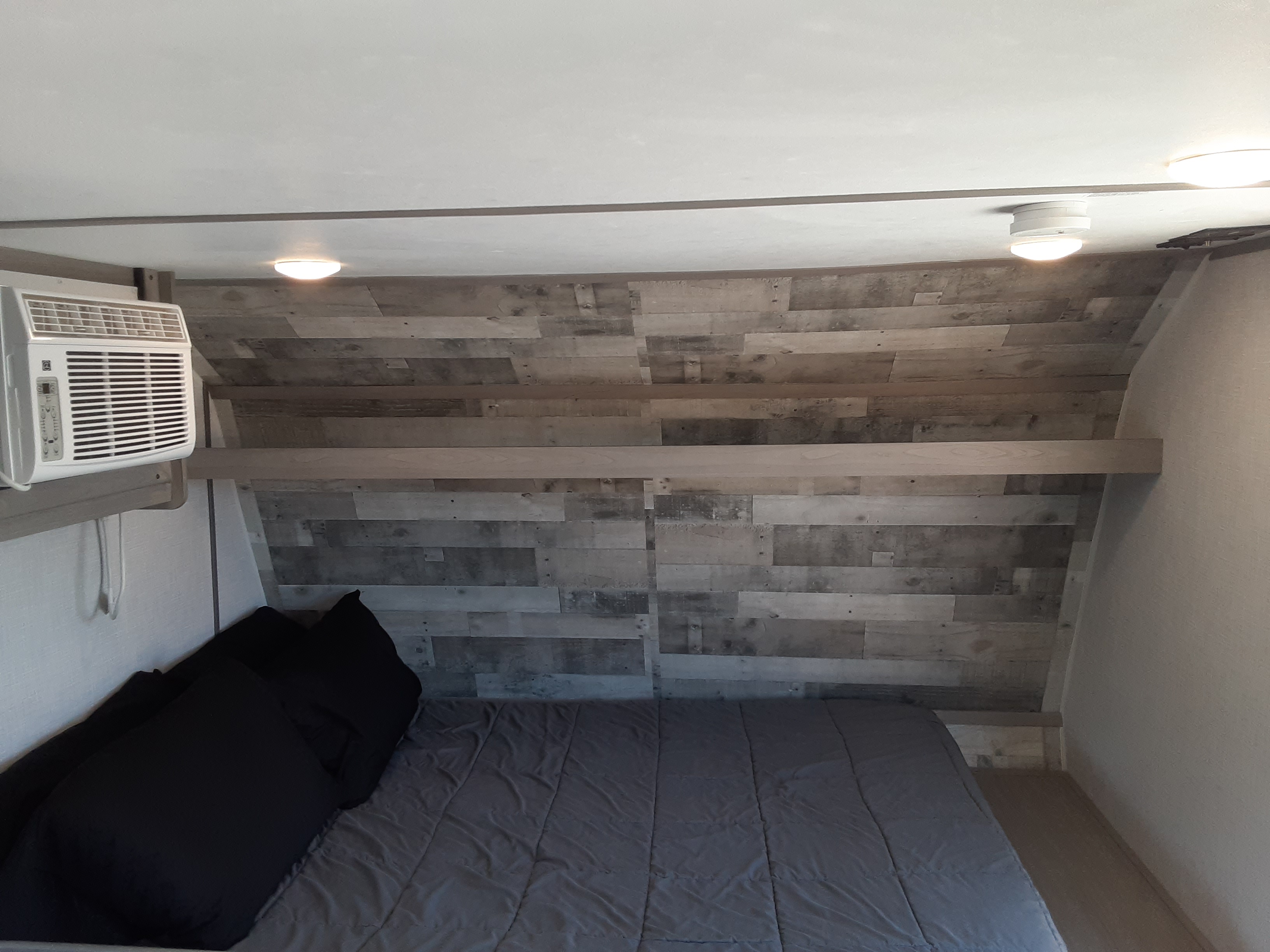 Cozy RV rental bedroom with a large bed, distressed wood accent wall, and a convenient air conditioner unit.. Coleman Other 2022