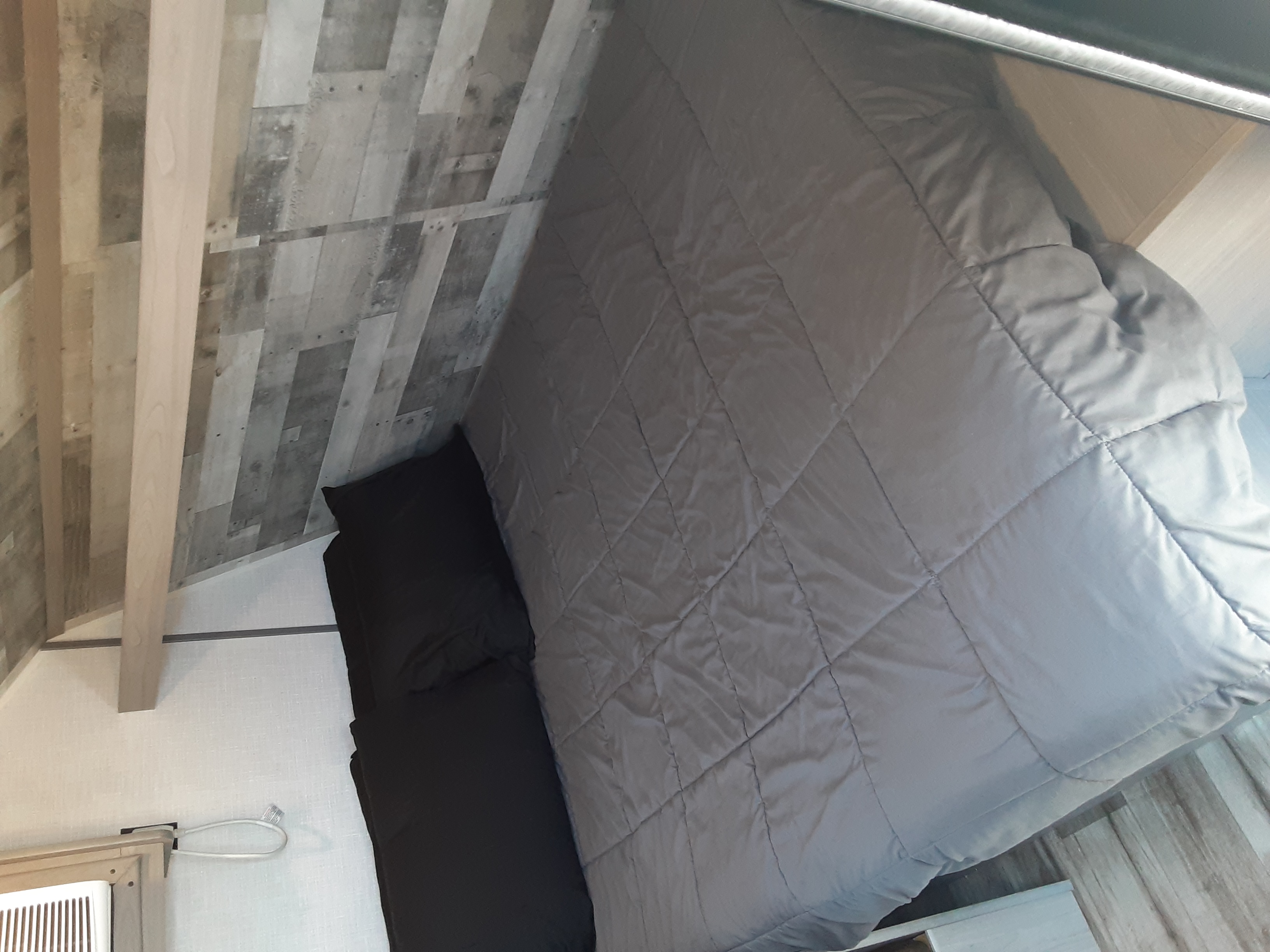 RV rental bedroom: a cozy, compact space with a grey quilted bed, black pillow, and angled wood plank ceiling.. Coleman Other 2022