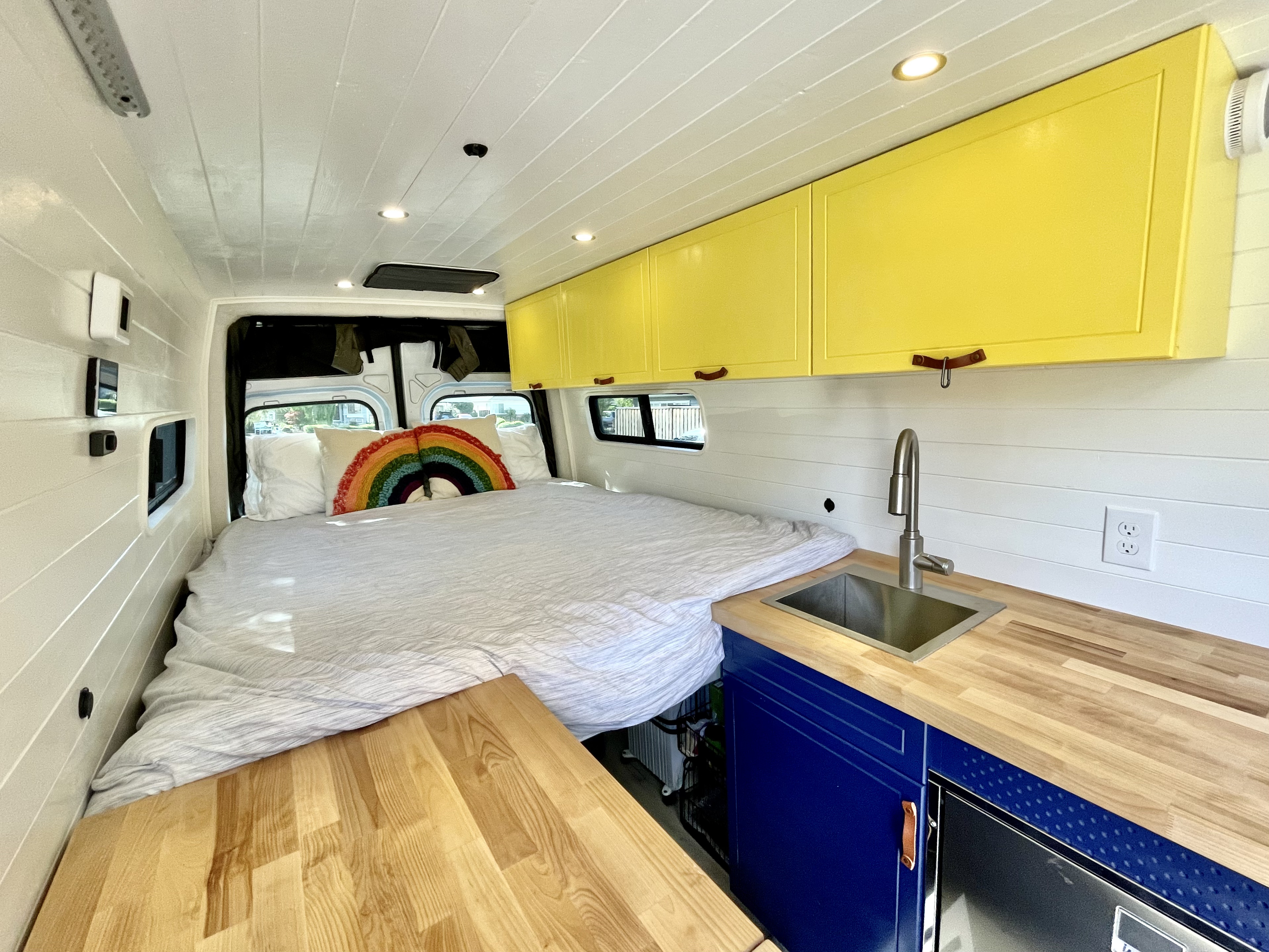 Cozy RV rental van interior features a bed, bright yellow cabinets, a mini-kitchen with sink, and fridge.. Mercedes-Benz sprinter 2020
