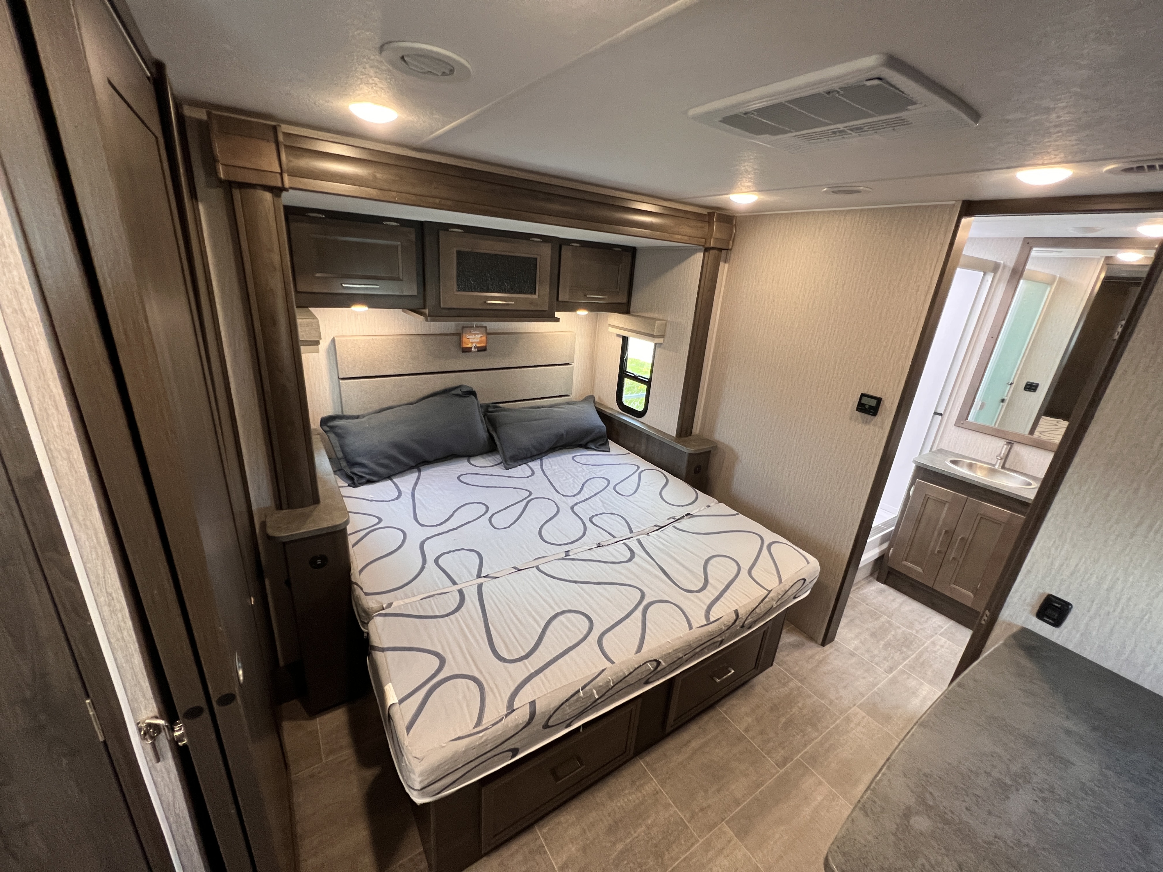 An RV rental bedroom featuring a large bed, modern built-in storage, bright lighting, and a view into the compact bathroom.. Coachmen Mirada 2022