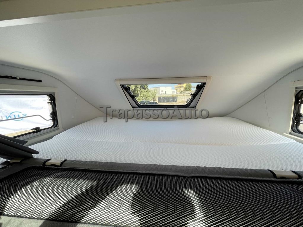 Interior of an RV rental sleeping area featuring a large white mattress, surrounding windows, and a black mesh safety barrier.. SunLiving A 75 DP 2024