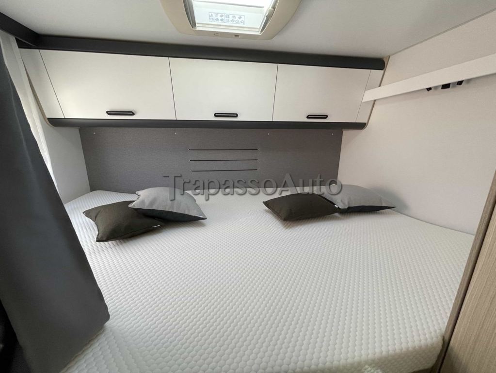 This compact camper van interior features a comfy bed, pillows, and overhead cabinets for an RV rental.. SunLiving A 75 DP 2024